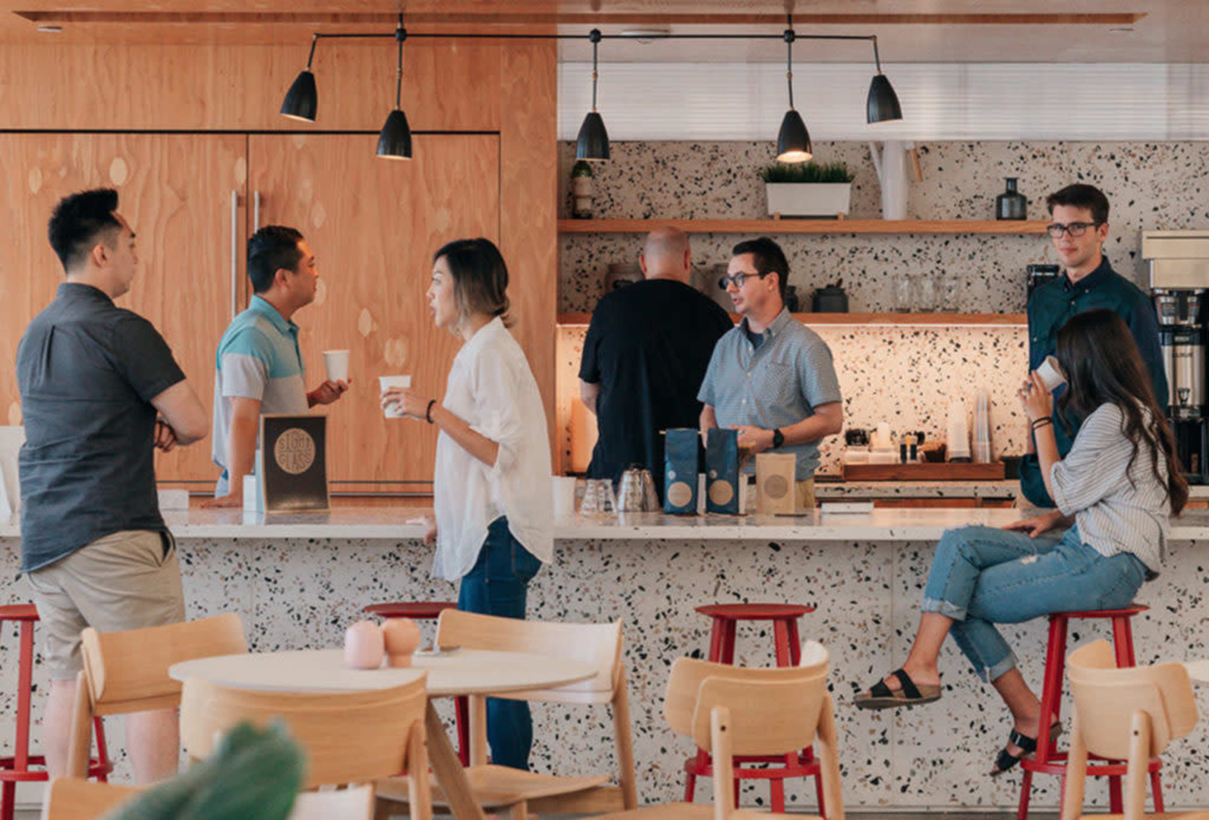 A group of people socializes in a modern café with a speckled wall and wooden accents.