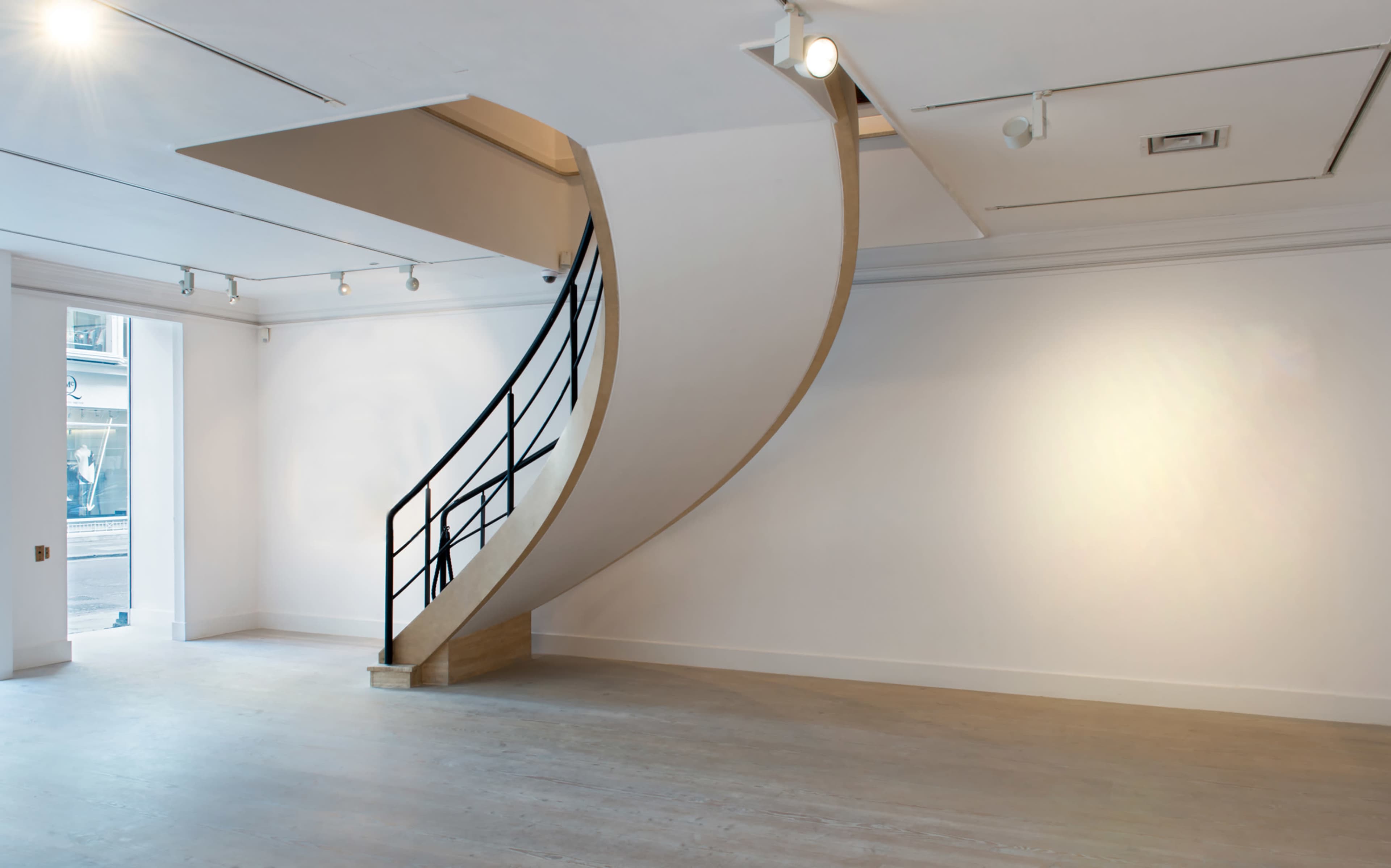 A modern, curved staircase leading from a minimalist, white-walled interior with track lighting.