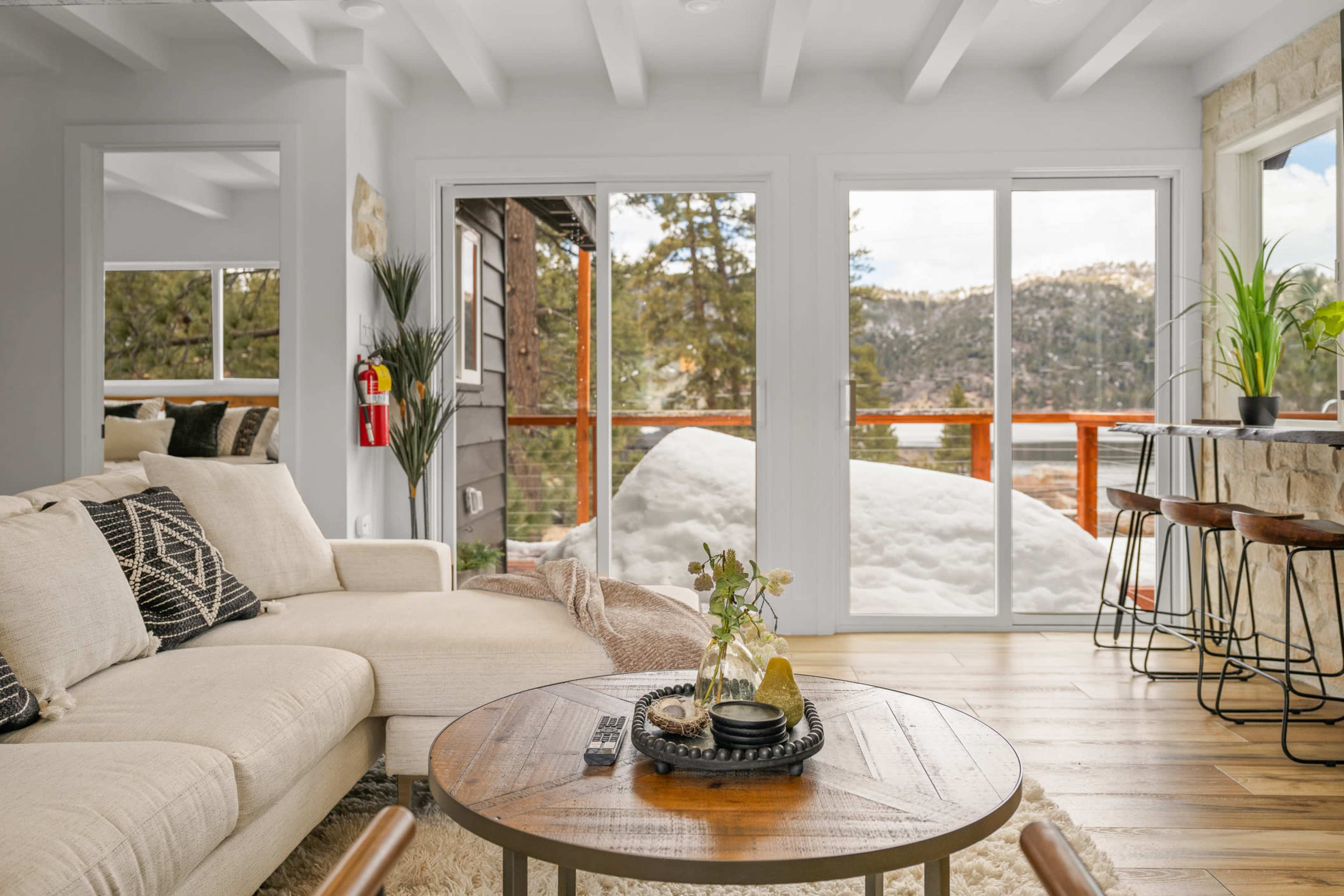 The cozy living room features a beige sectional sofa, a wooden coffee table with decorative items, and large windows that overlook snow-covered outdoor scenery.
