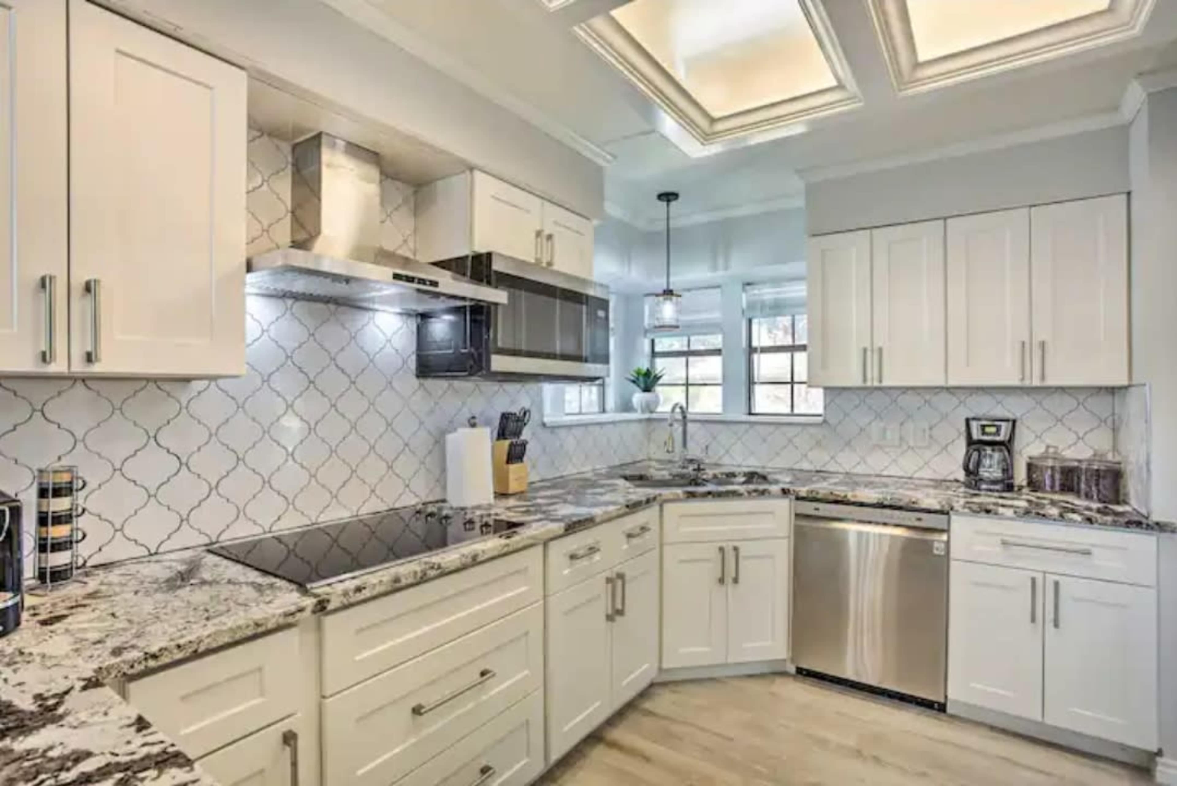 The image shows a modern kitchen with white cabinetry, a granite countertop, and stainless steel appliances.
