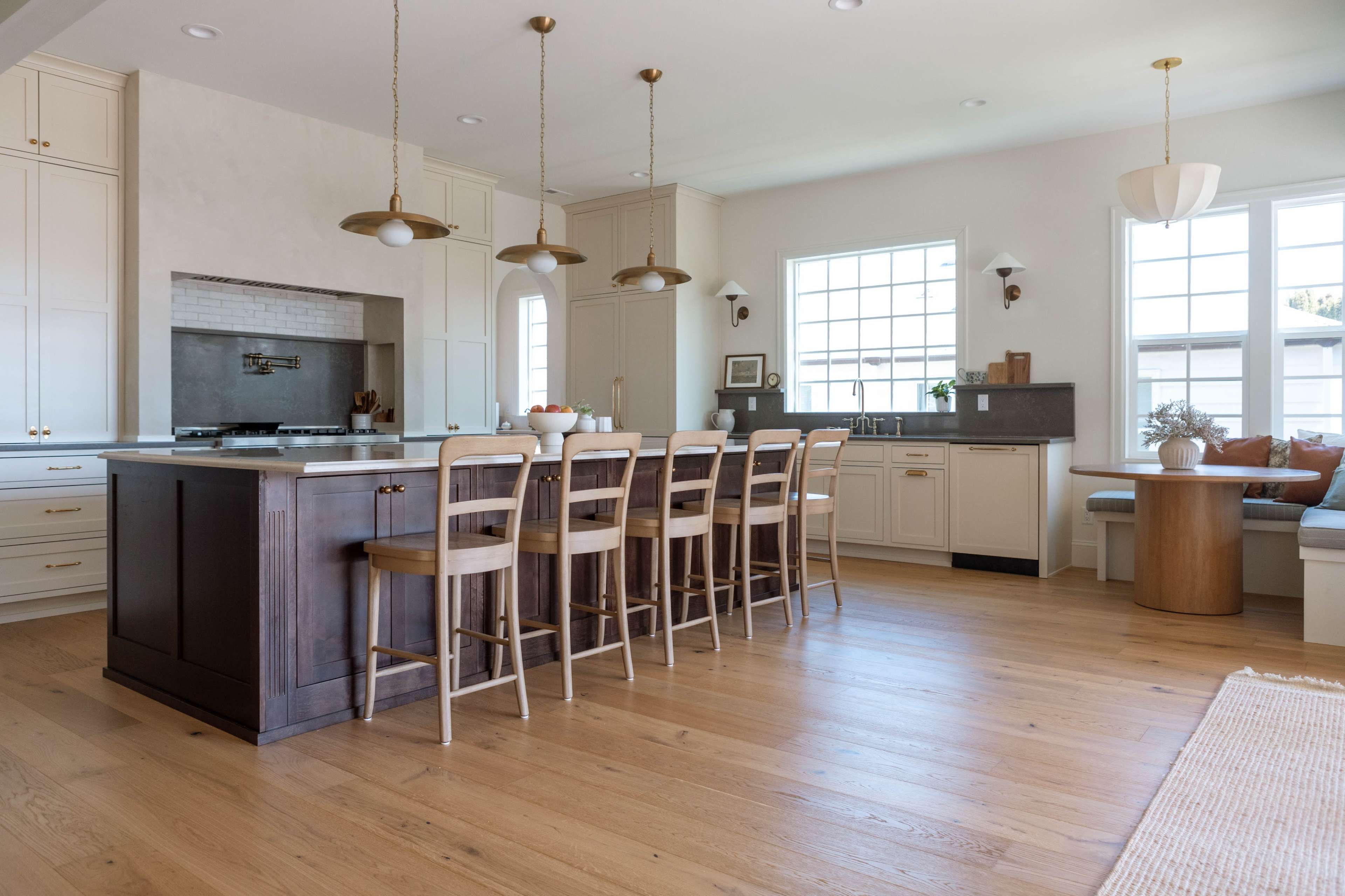 The image shows a spacious, modern kitchen with a large wooden island, bar stools, and ample natural light from the windows.