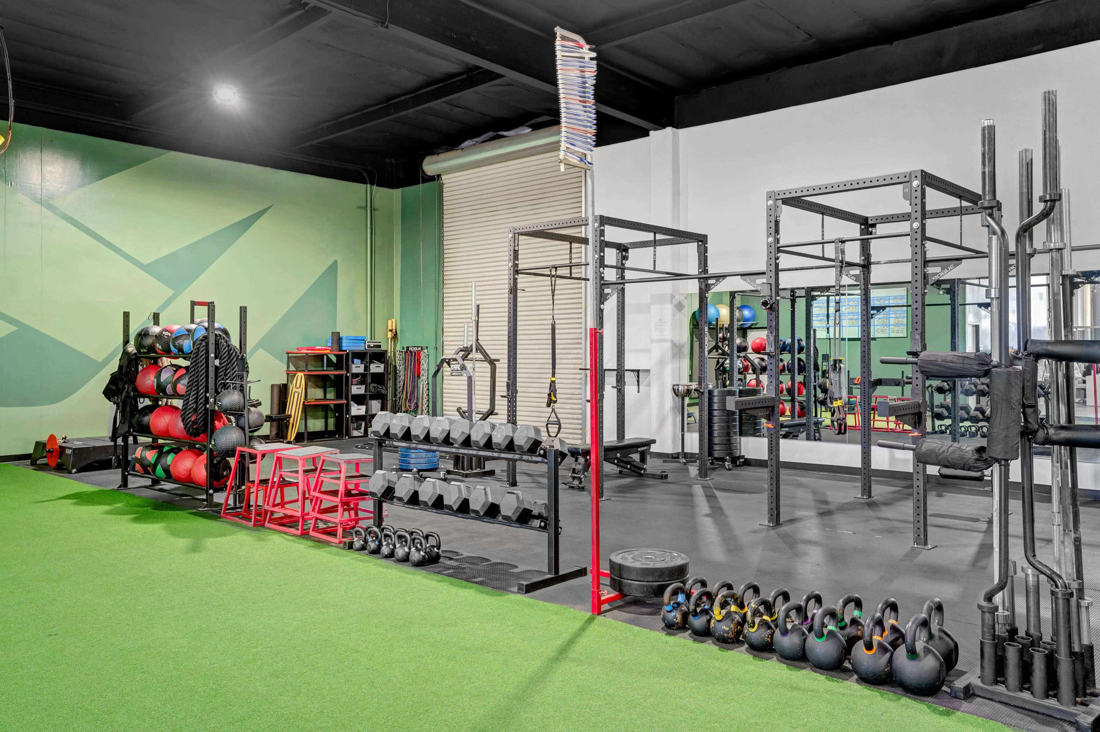 A gym interior featuring various exercise equipment, including dumbbells, kettlebells, and medicine balls, arranged on a rubber floor.