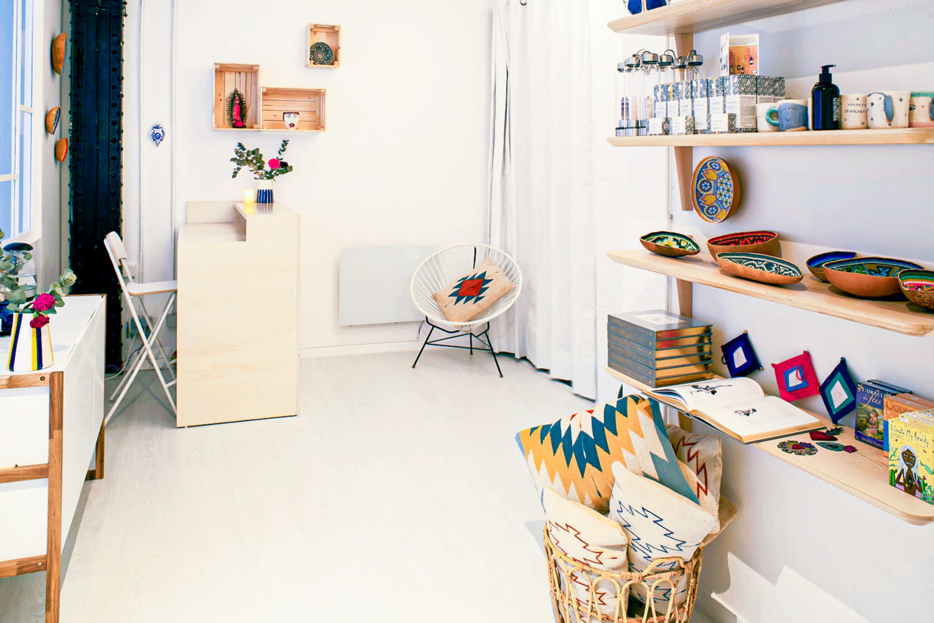 A bright, modern interior features a wooden shelf with decorative items, a small desk area, and a cozy chair amidst a clean, minimally decorated space.