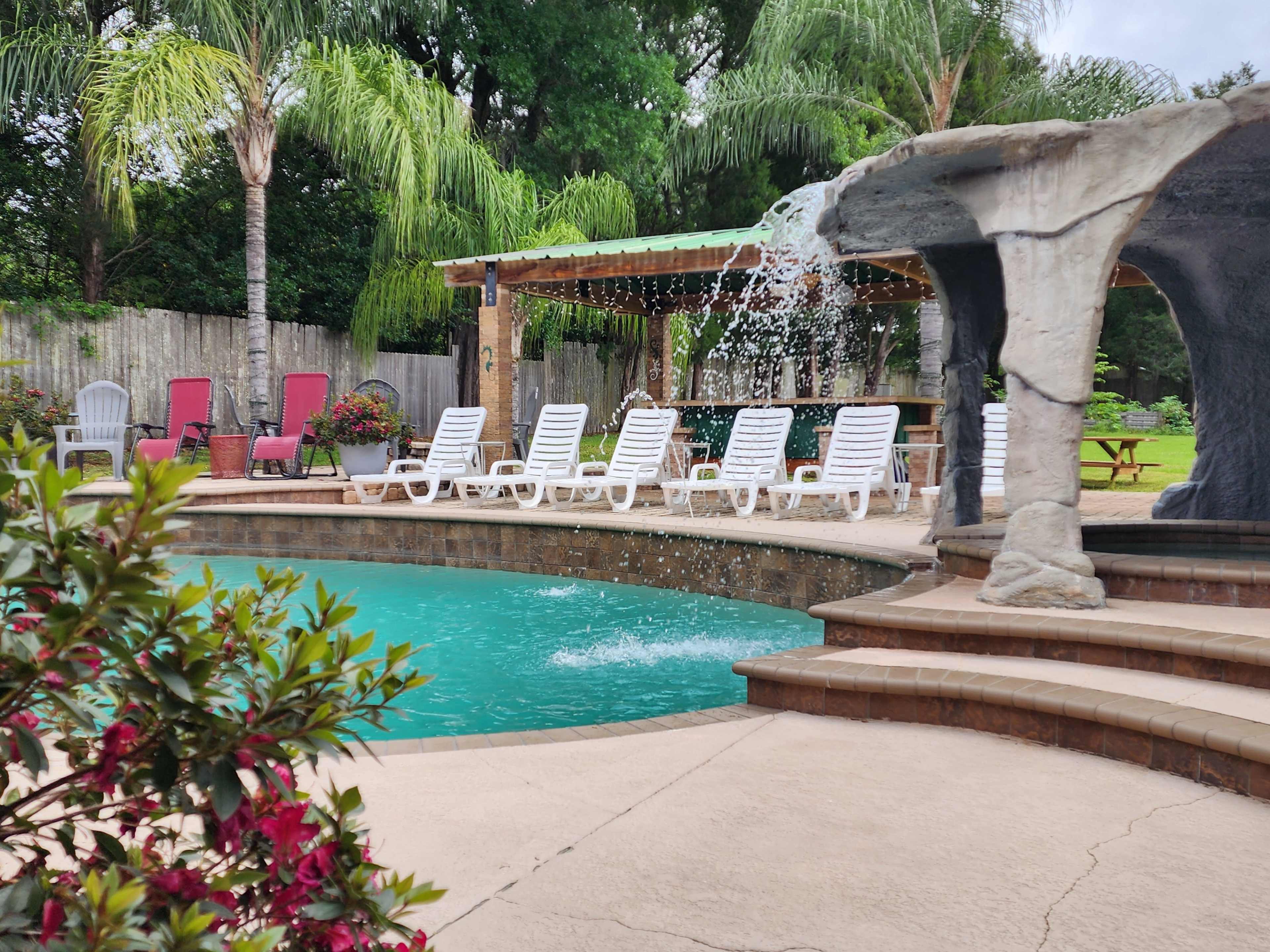 A pool area features a cascading fountain, surrounded by lounge chairs and lush greenery.