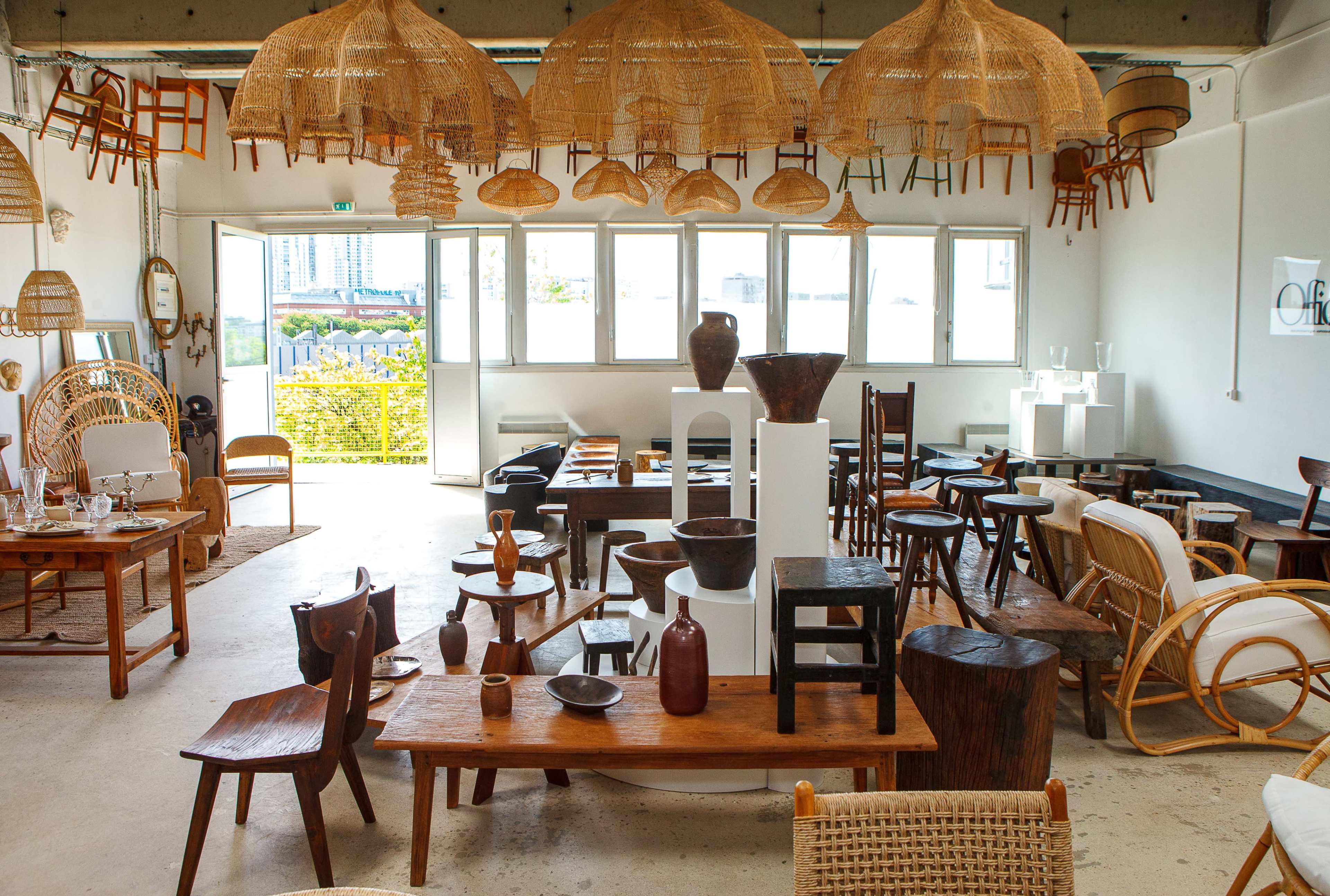 A spacious interior filled with various wooden furniture pieces, decorative objects, and hanging woven light fixtures.