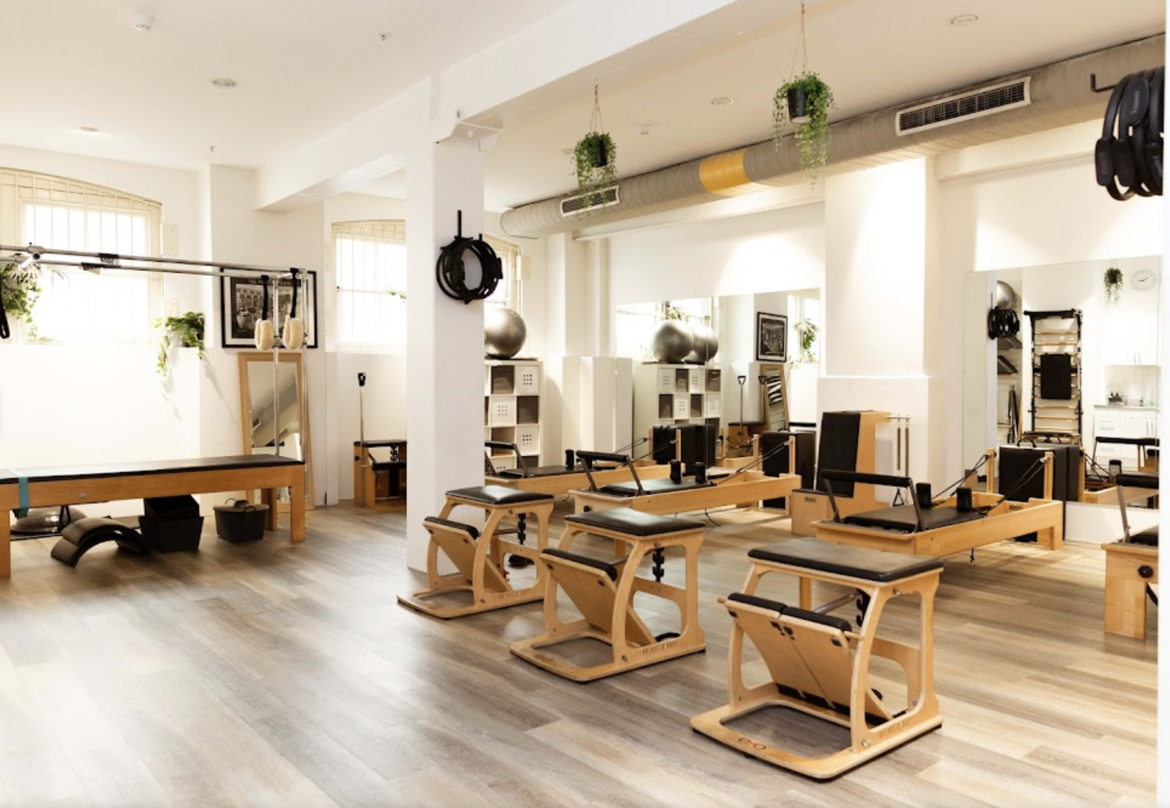 A modern Pilates studio with several Reformer machines arranged neatly along wooden flooring and large mirrors reflecting the space.