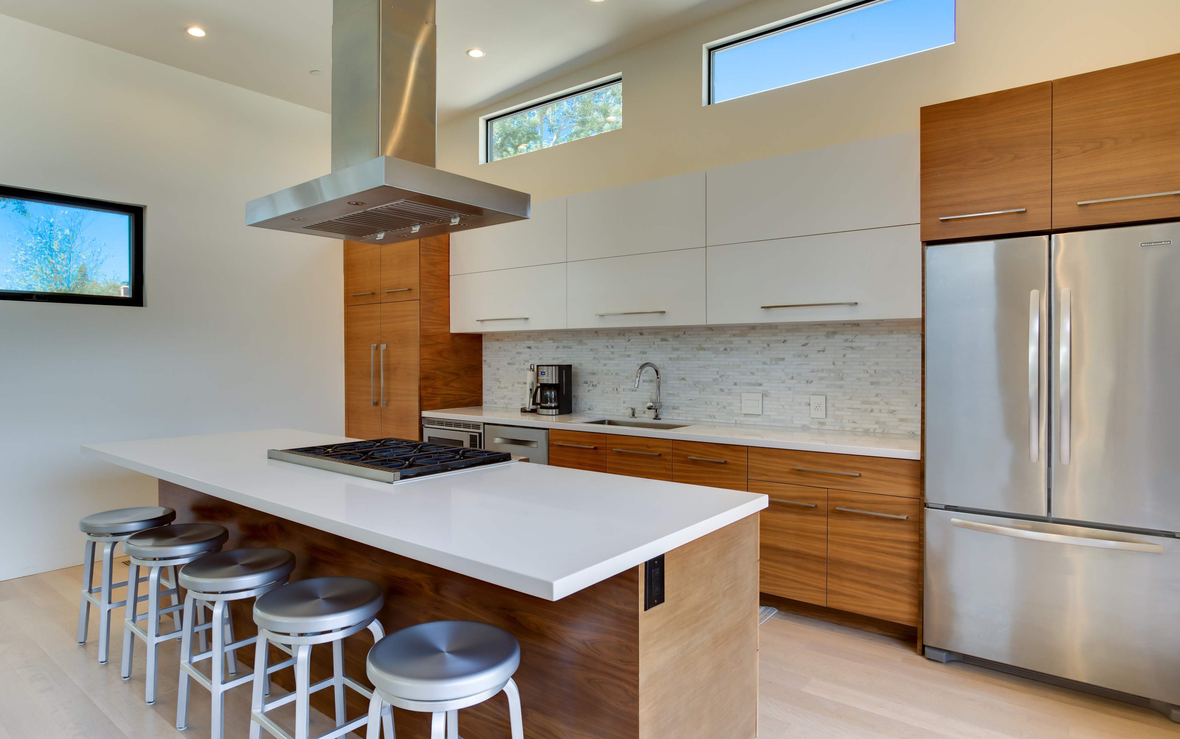 The image shows a modern kitchen with a central island, stainless steel appliances, and wooden cabinetry.