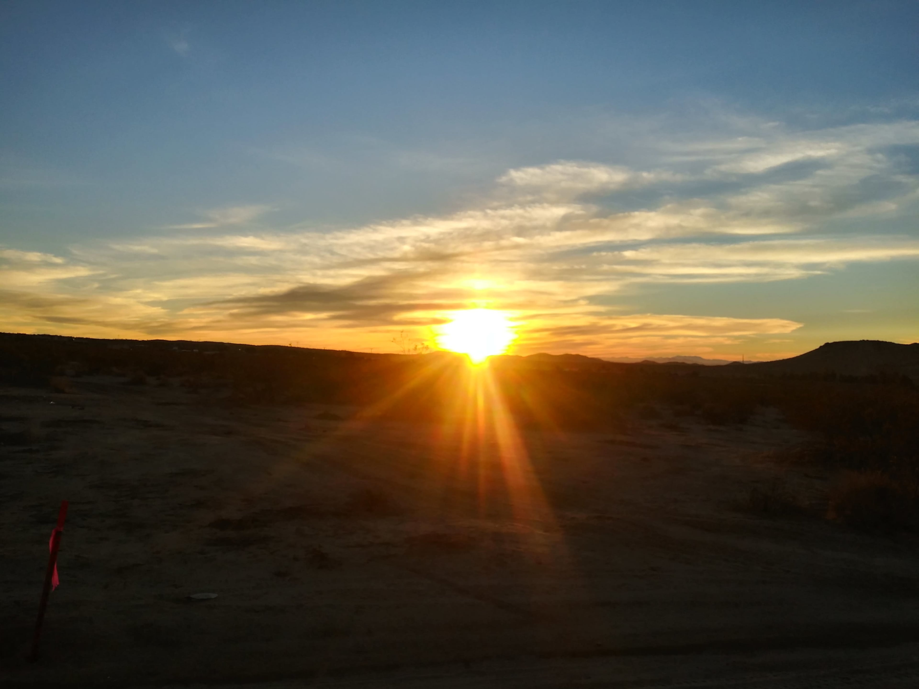 The sun sets over a barren landscape, casting rays of light across the sky.