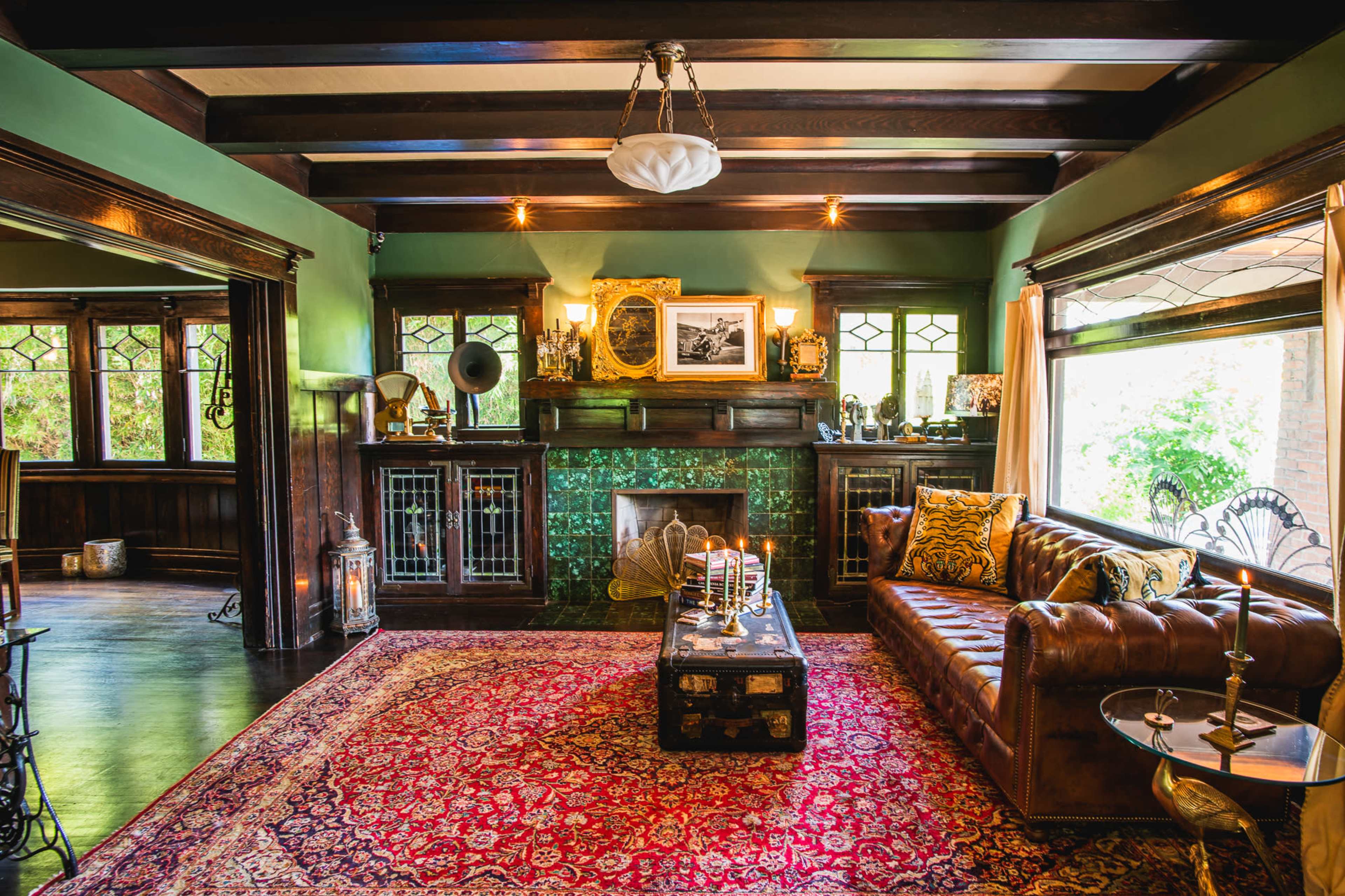 A warmly lit living room featuring a brown leather sofa, a vintage fireplace, and an ornate area rug on the wooden floor.