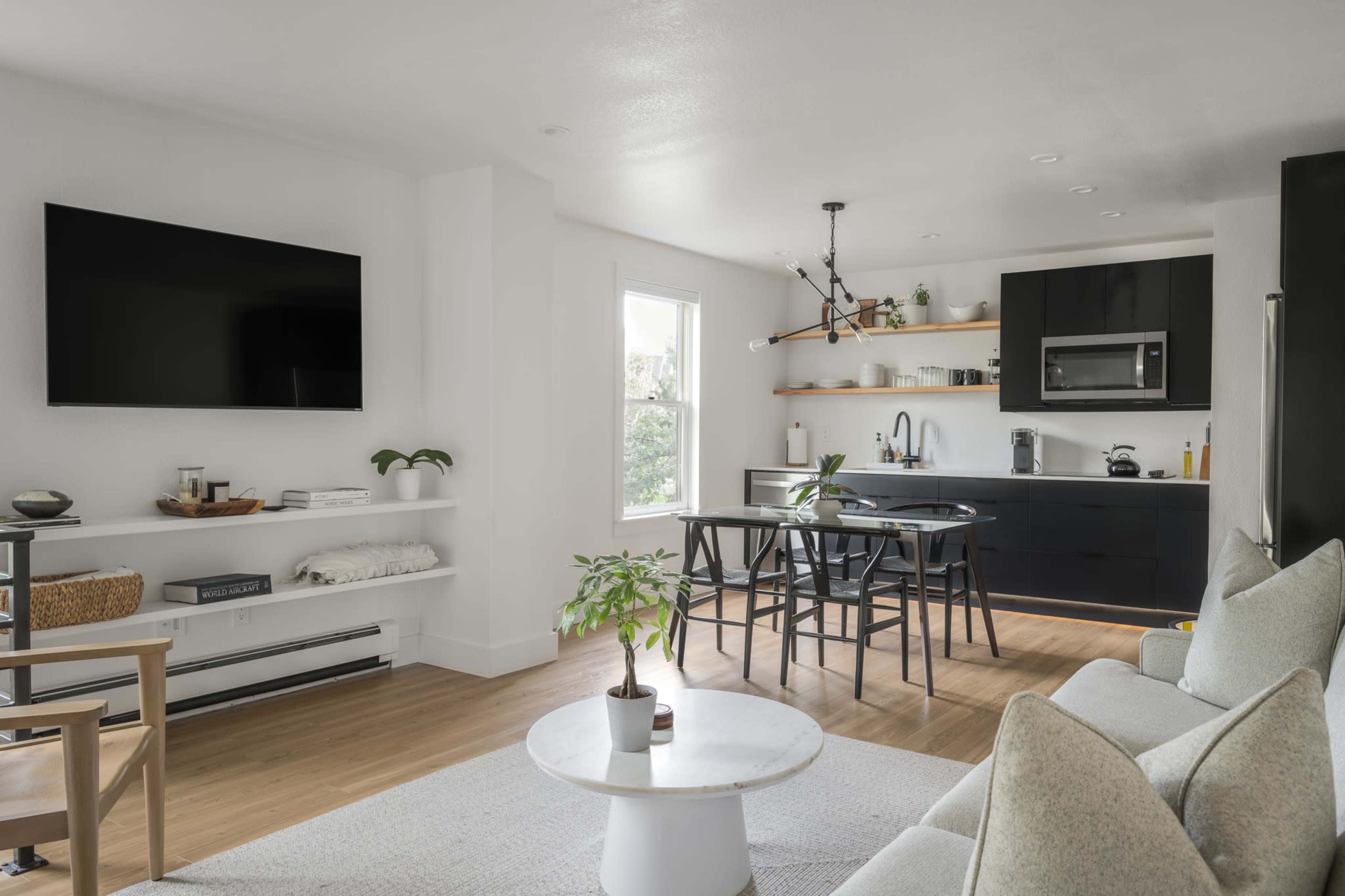 A modern, open-concept living space featuring a living area with a television, a sleek kitchen, and a dining area with a circular table and chairs.