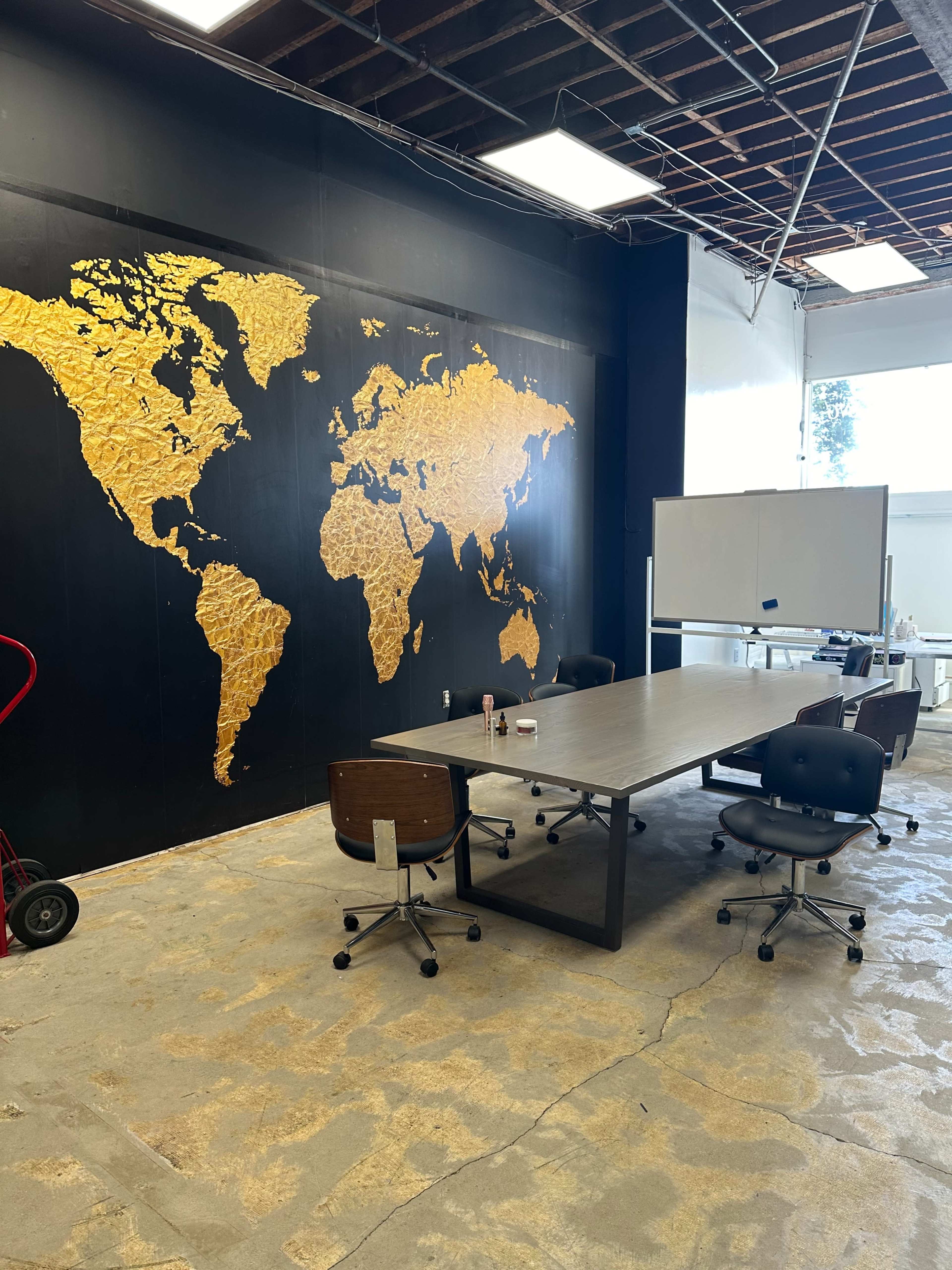 A meeting room with a large golden world map on a black wall, a central table, and several office chairs arranged around it.