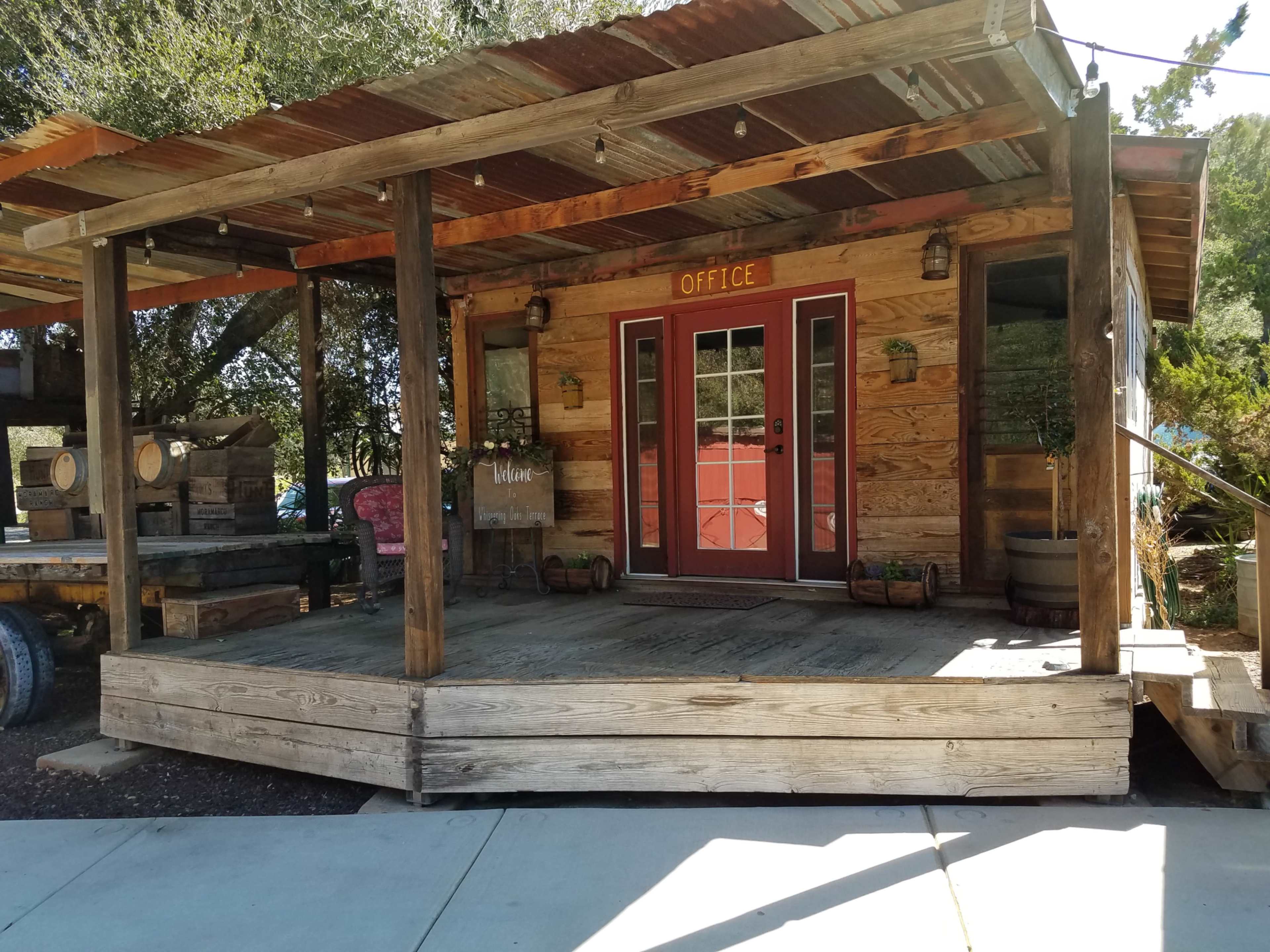The image shows a wooden cabin with a front porch, labeled "OFFICE," featuring double doors and surrounding greenery.