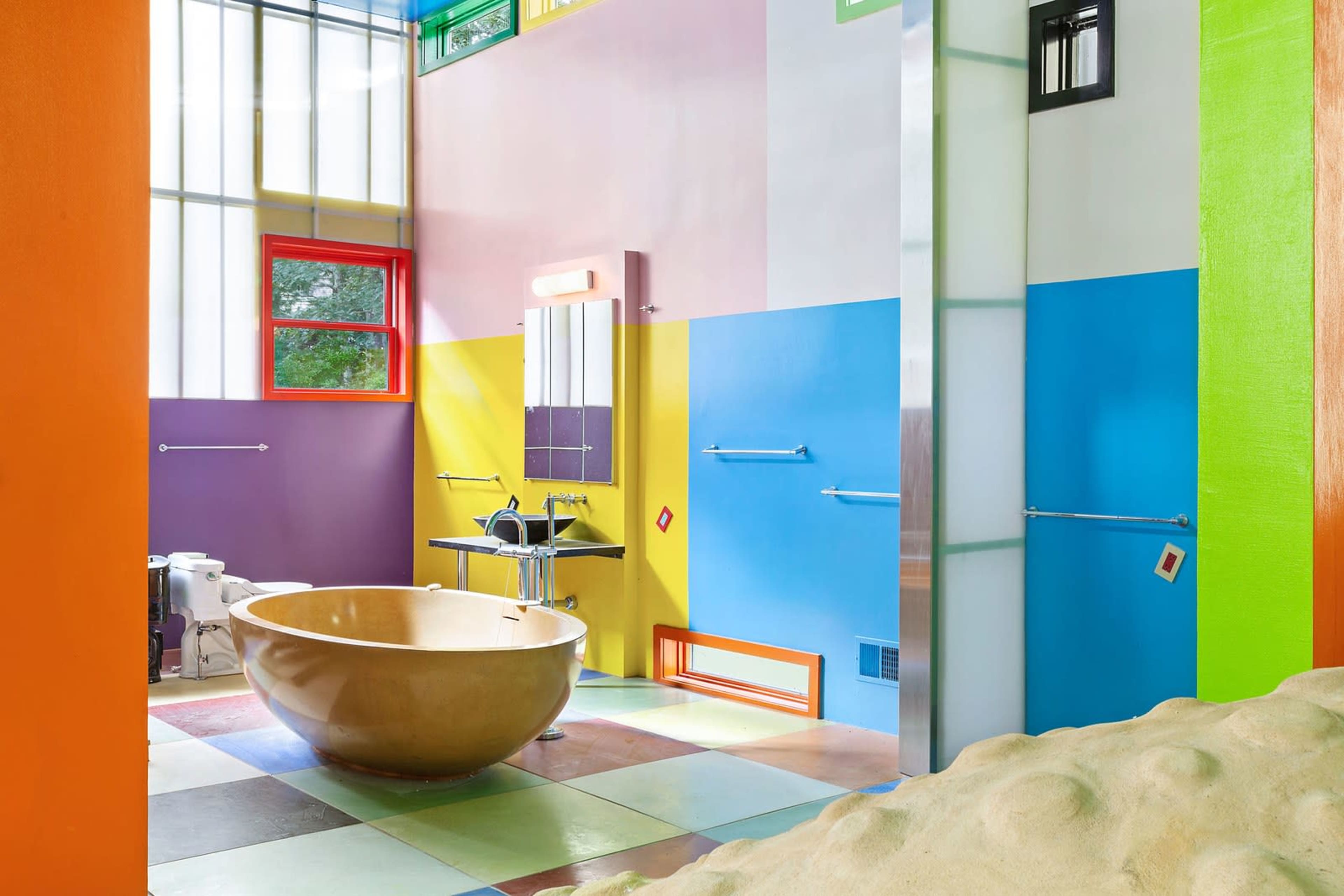 The image shows a colorful bathroom featuring a rounded bathtub, vibrant walls in assorted shades, and a modern sink area.