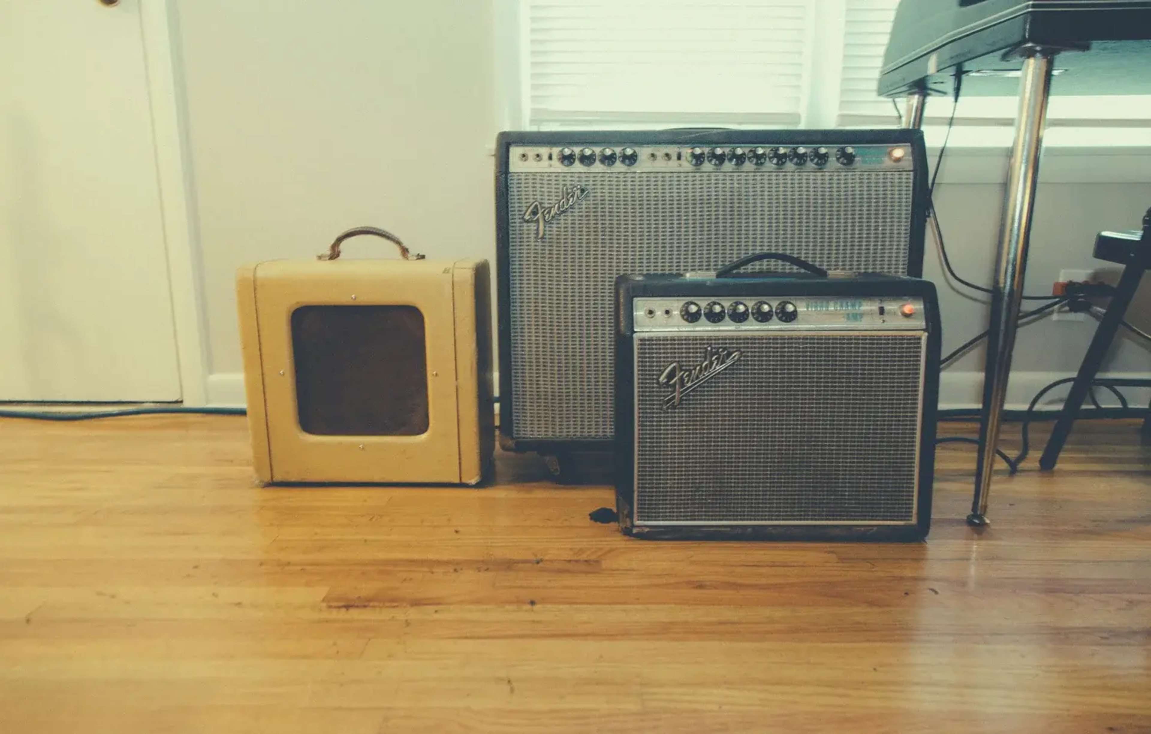 The image shows three guitar amplifiers arranged on a wooden floor near a window.