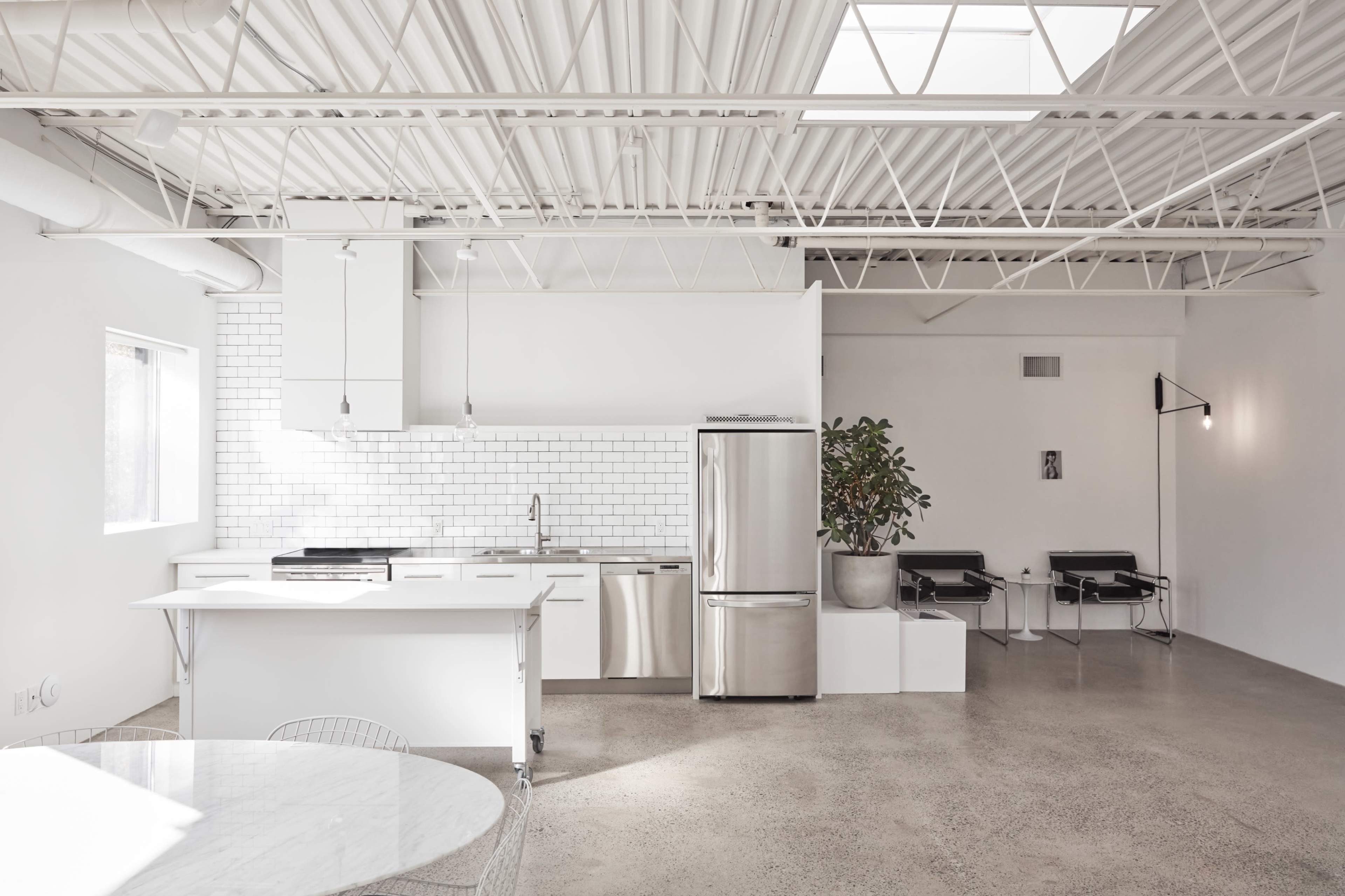 A modern, open-concept kitchen with stainless steel appliances, a white tile backsplash, and a concrete floor.