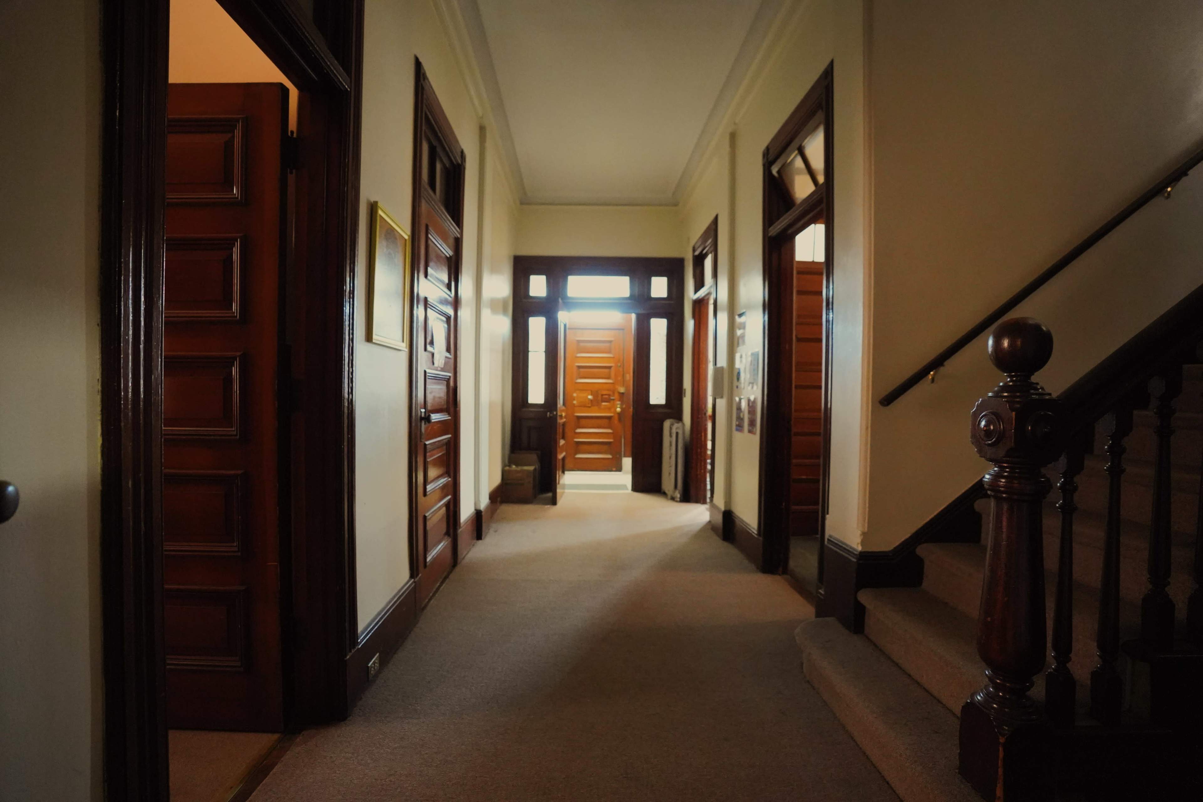 A well-lit hallway with wooden doors and a staircase on the right side.
