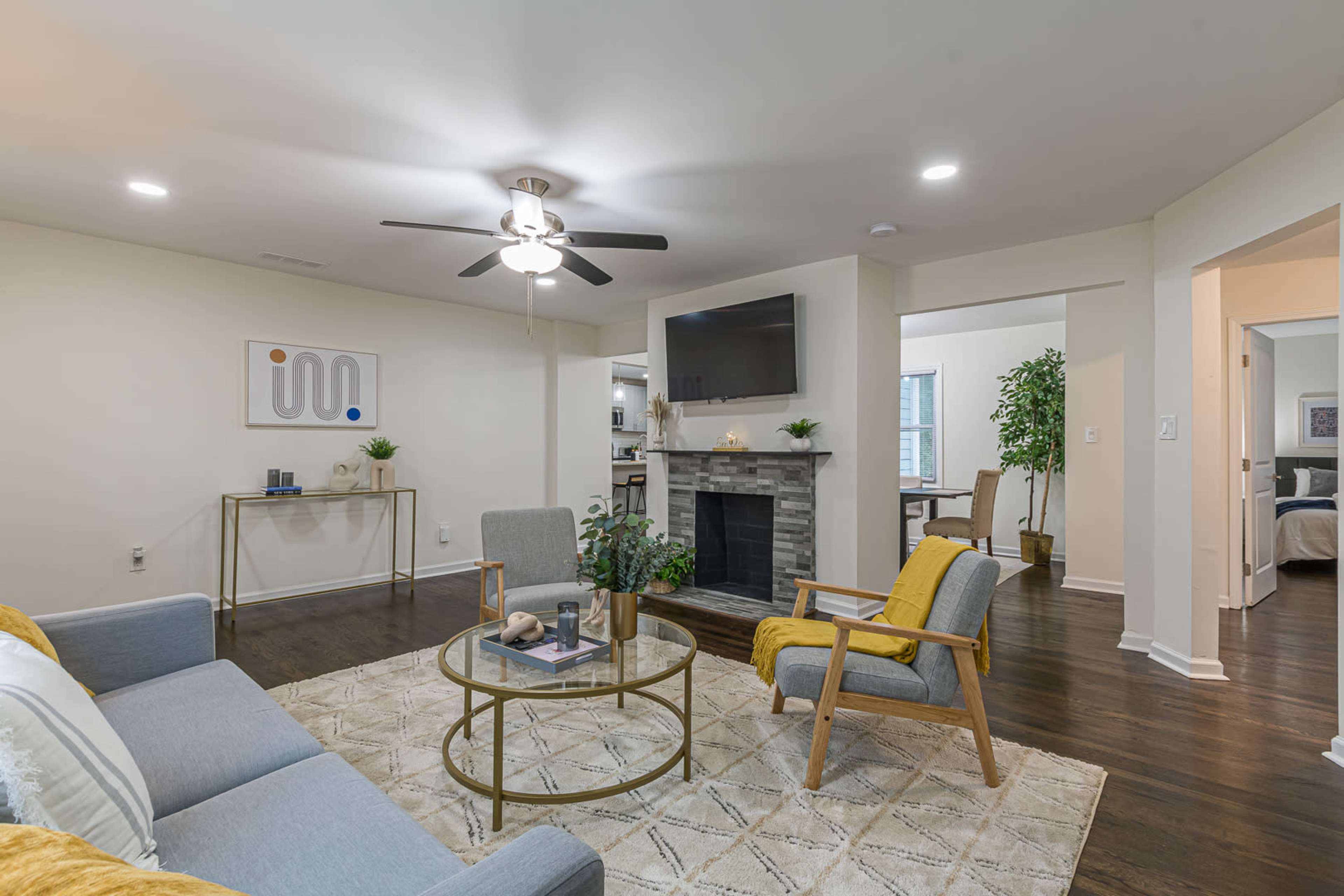 A modern living room with a sectional sofa, a coffee table, a stone fireplace, and an arranged space leading to a dining area.