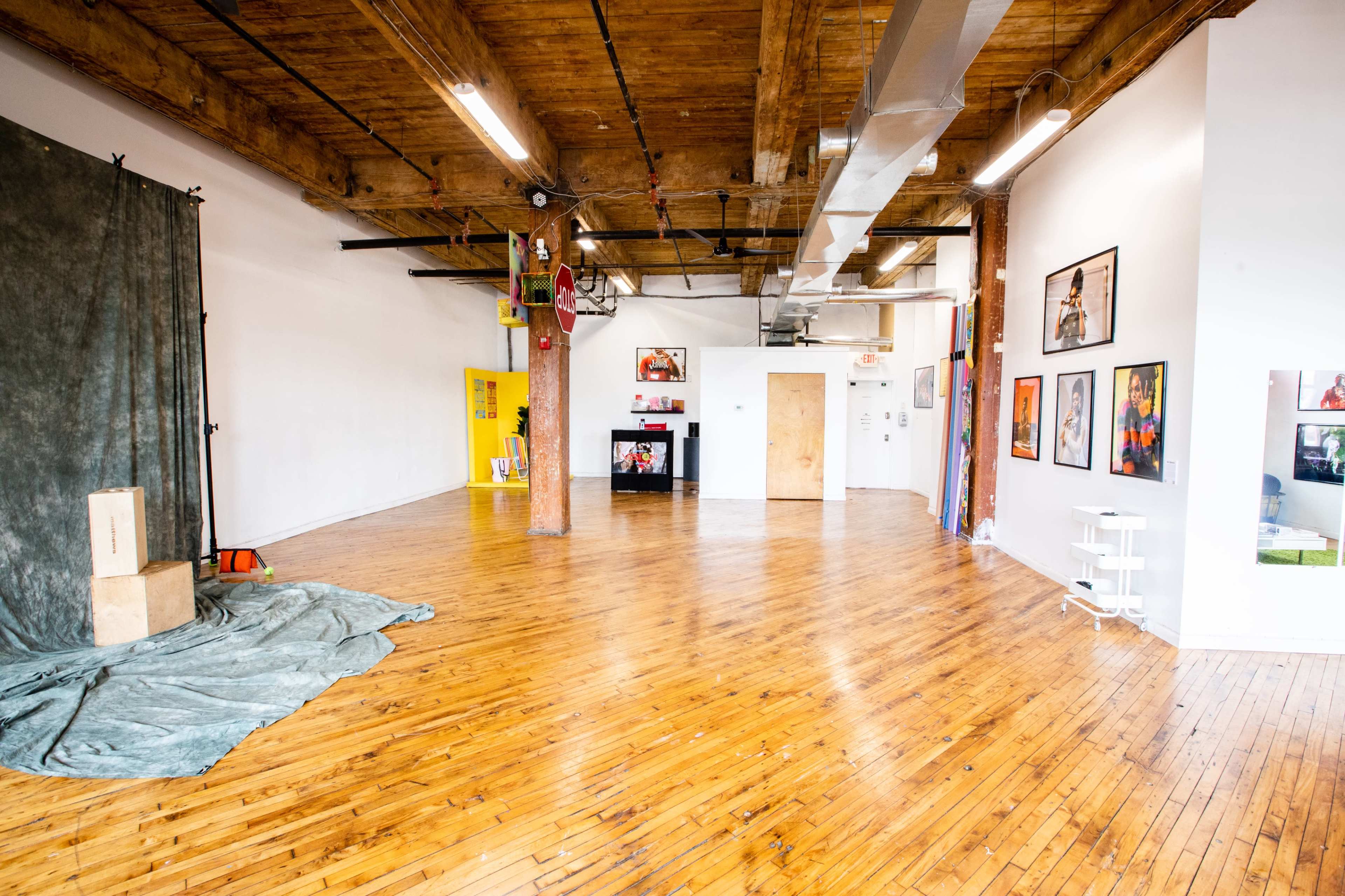 A spacious room with wooden floors, a backdrop draped on the left, and several framed pictures hanging on the walls.