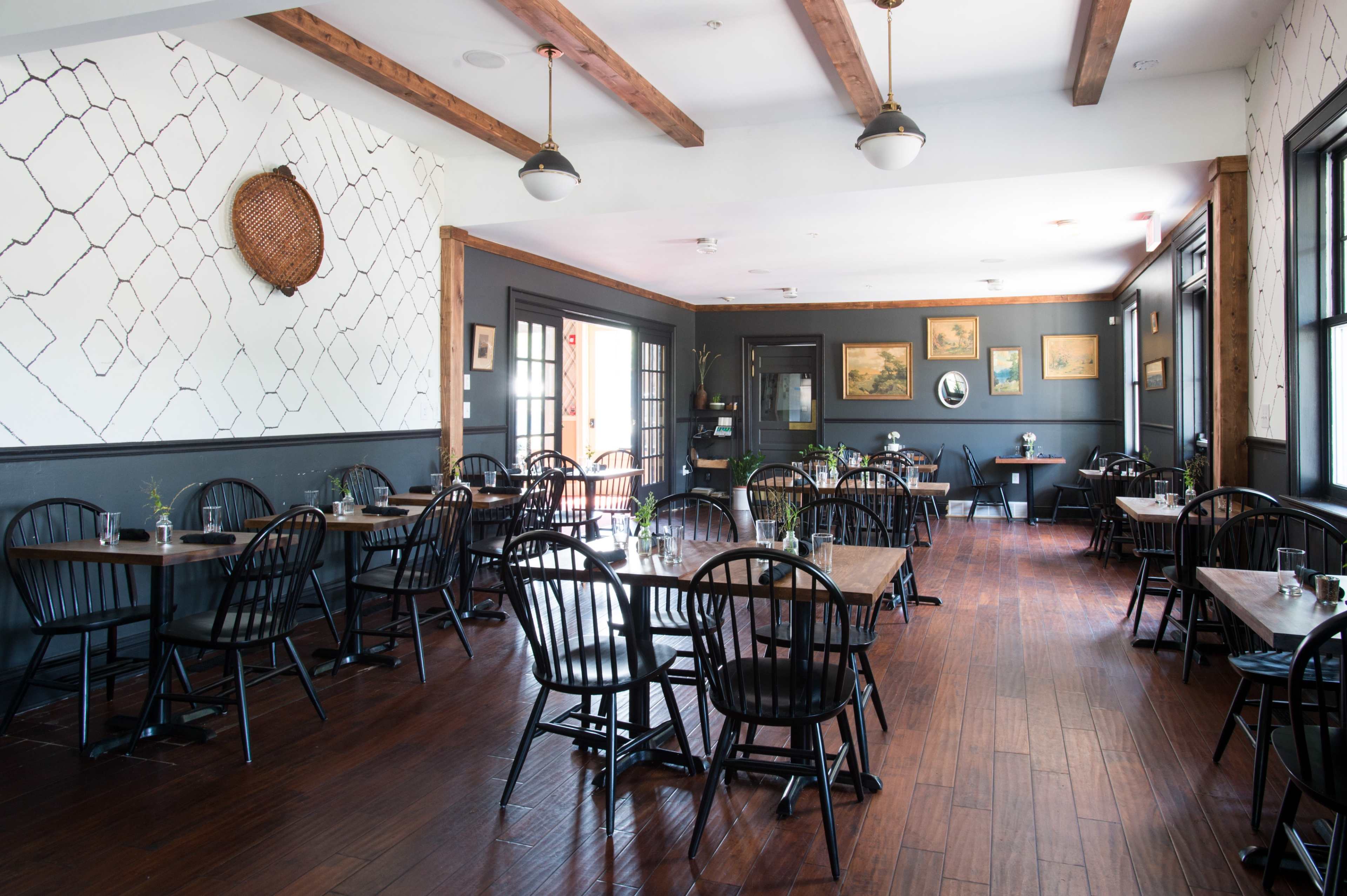 An empty restaurant interior featuring wooden tables, black chairs, and decorative wall art.