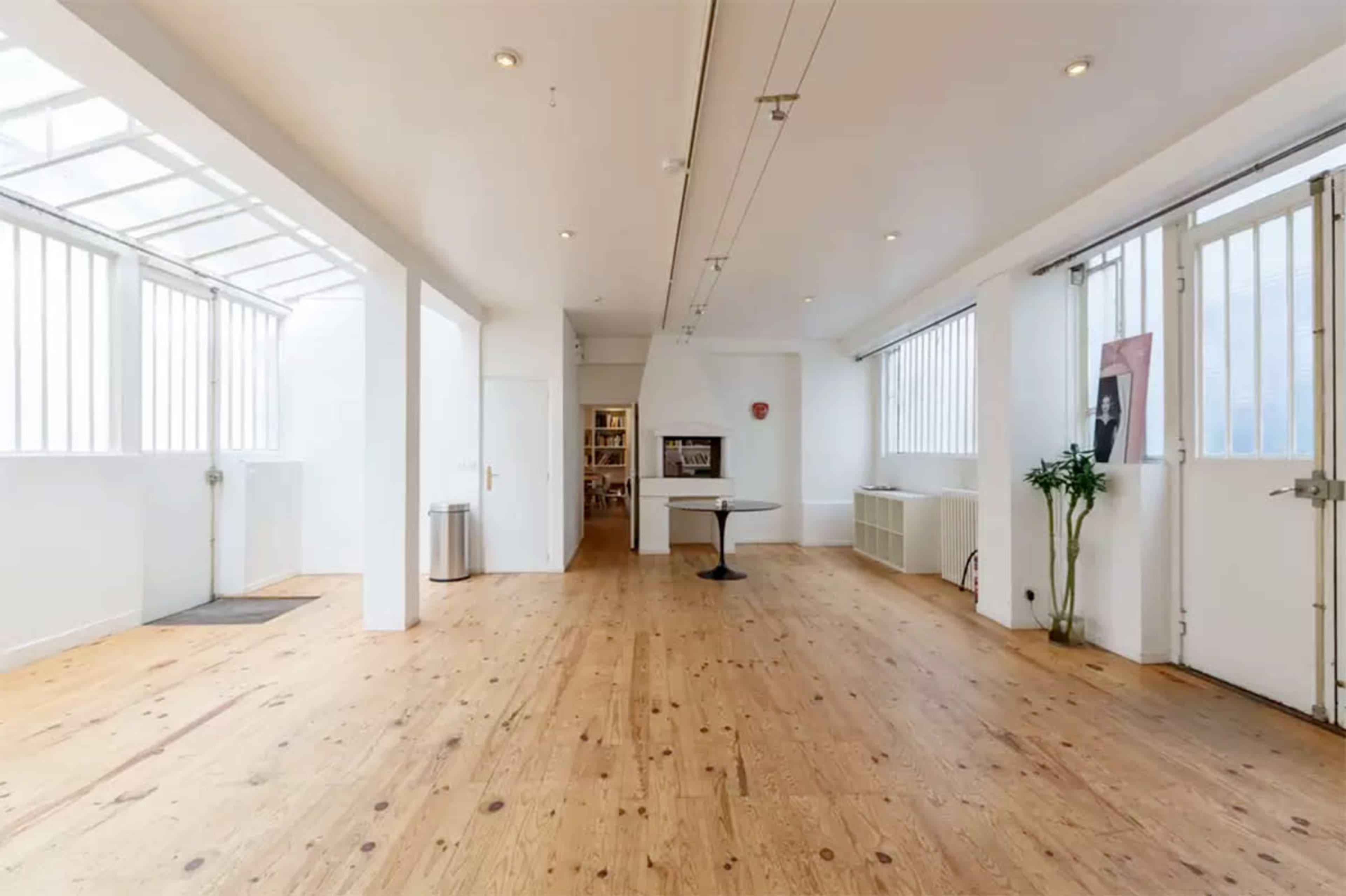 A spacious, empty room with wooden floors, large windows, and doors on either side.