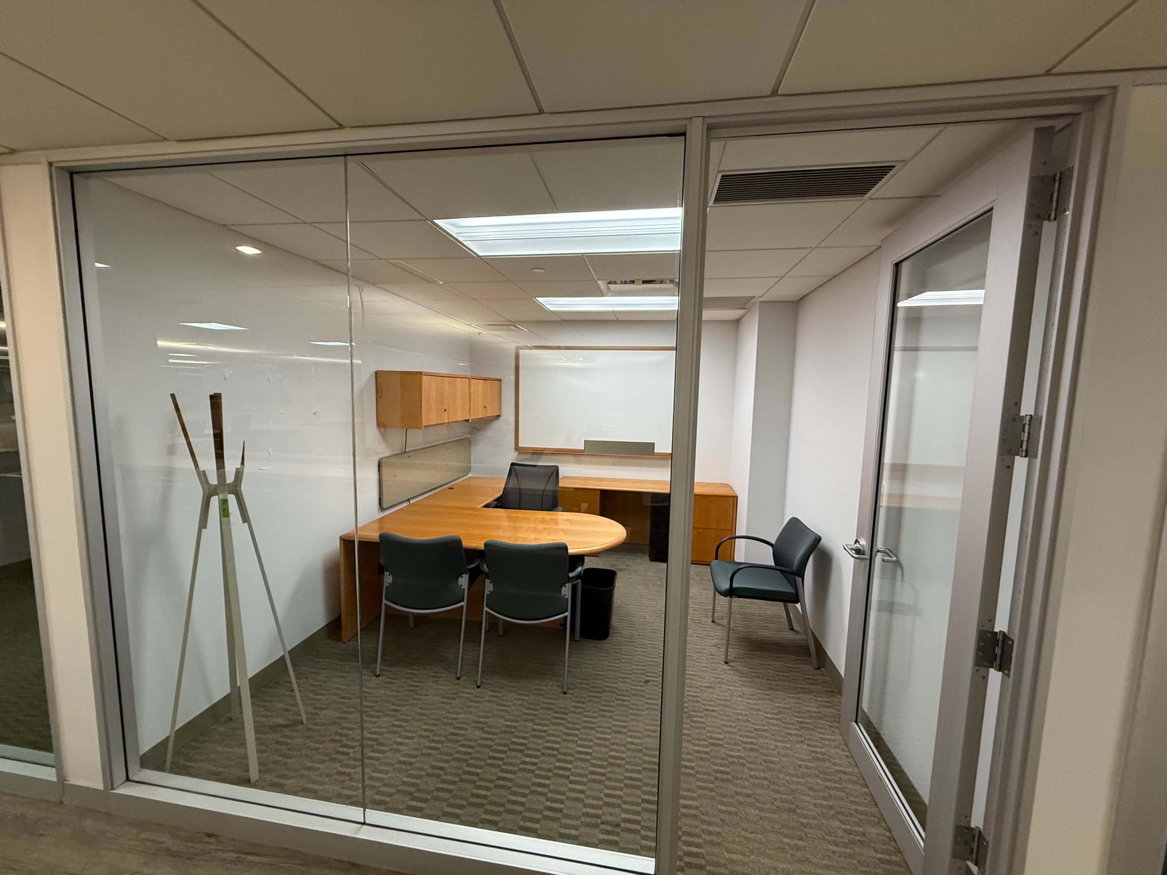 The image shows a modern glass-walled office with a large wooden meeting table, several chairs, and a whiteboard.