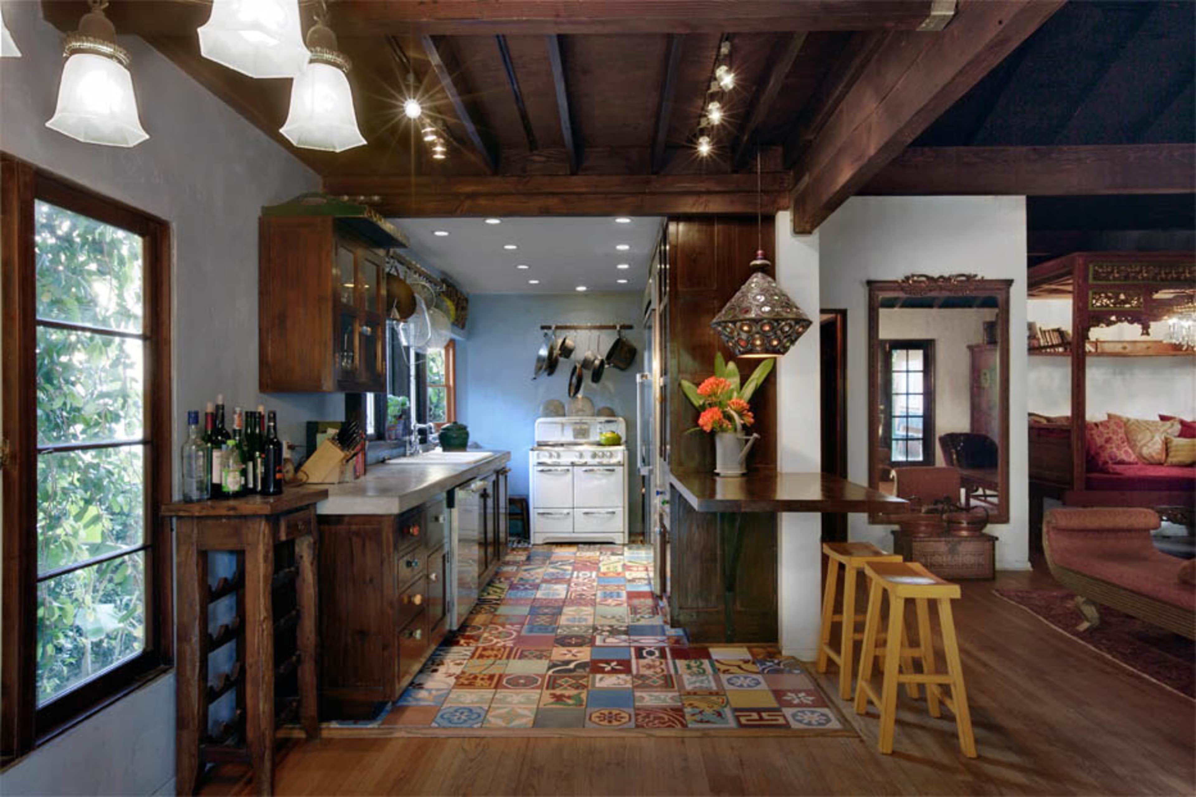 A rustic kitchen with wooden cabinets, a tiled floor featuring colorful patterns, and a small dining area with a bar and stools.