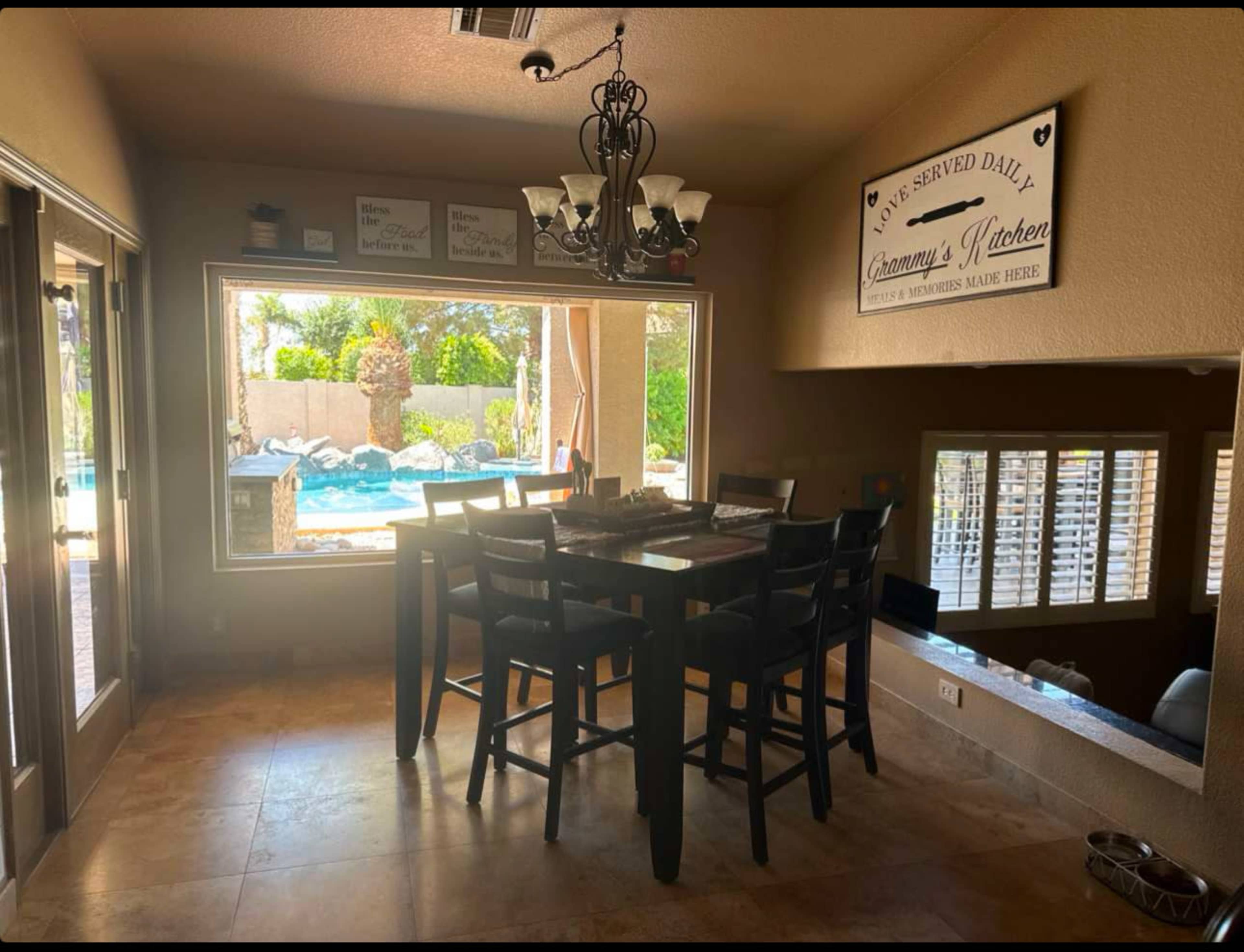 A dining area features a large table with high-backed chairs and a window overlooking a pool and patio area.