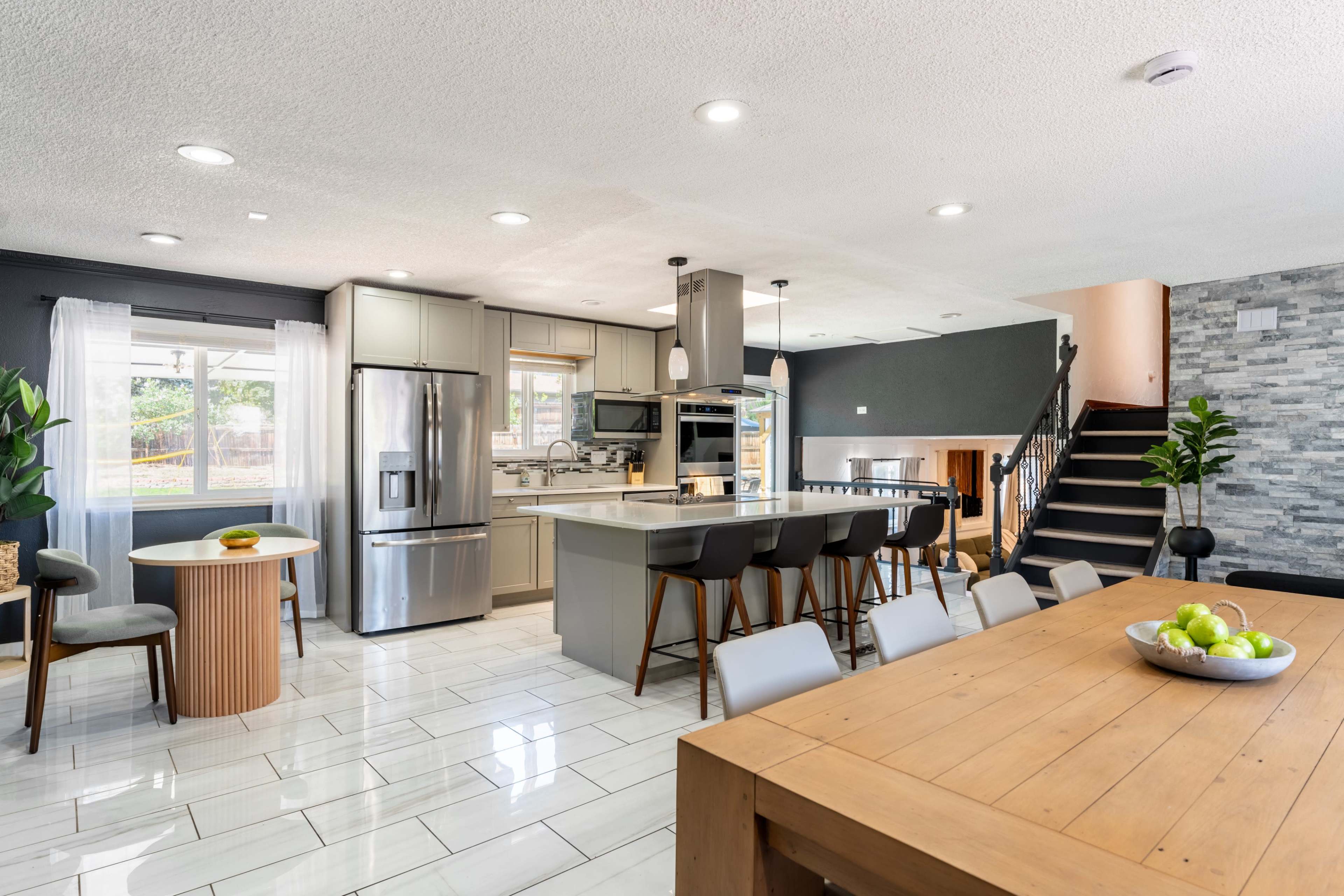 The image shows a modern kitchen and dining area with a dining table, chairs, and a staircase leading to another level.