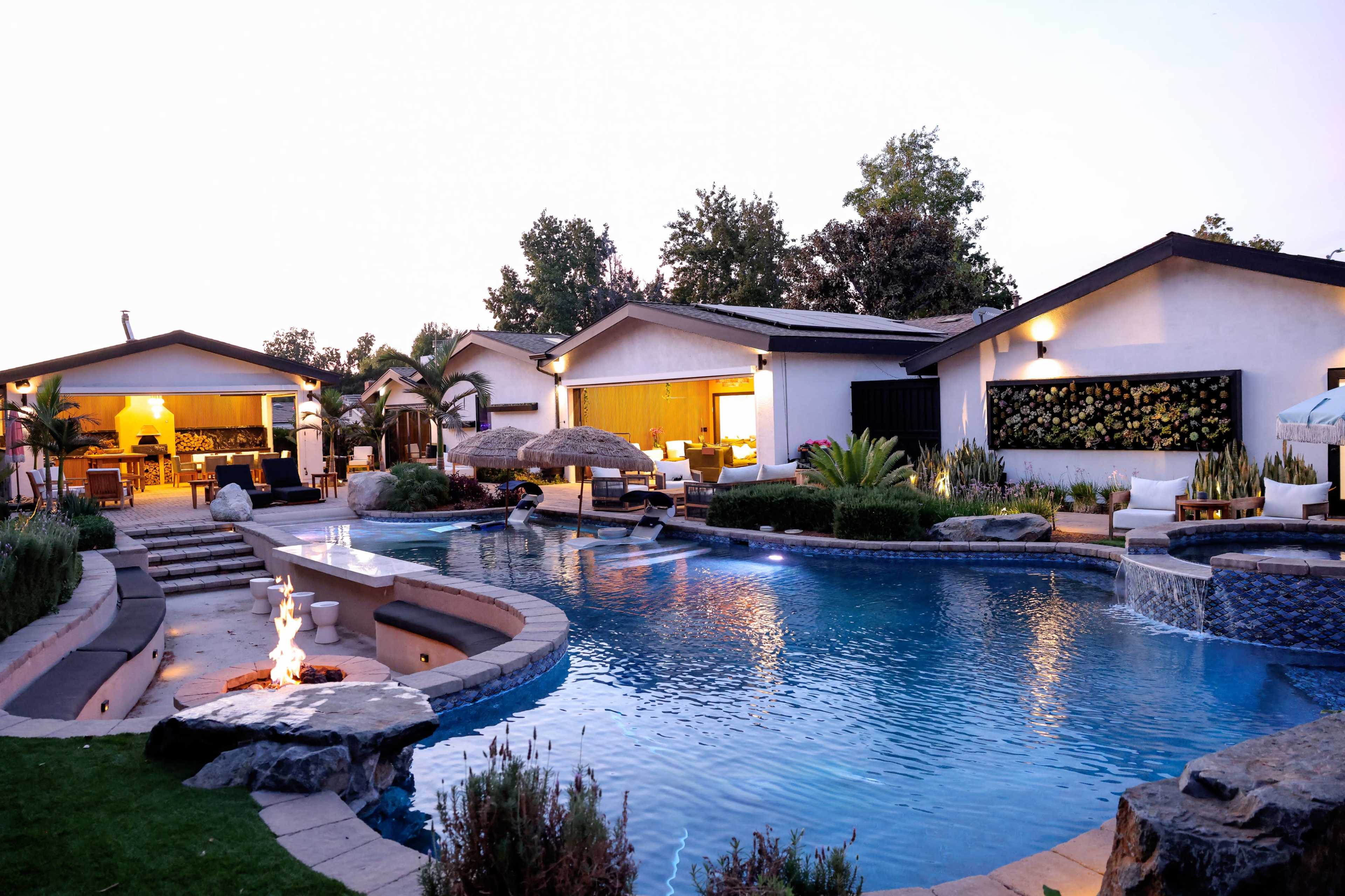 A luxurious residential property features a large swimming pool surrounded by landscaped gardens and modern outdoor seating areas.