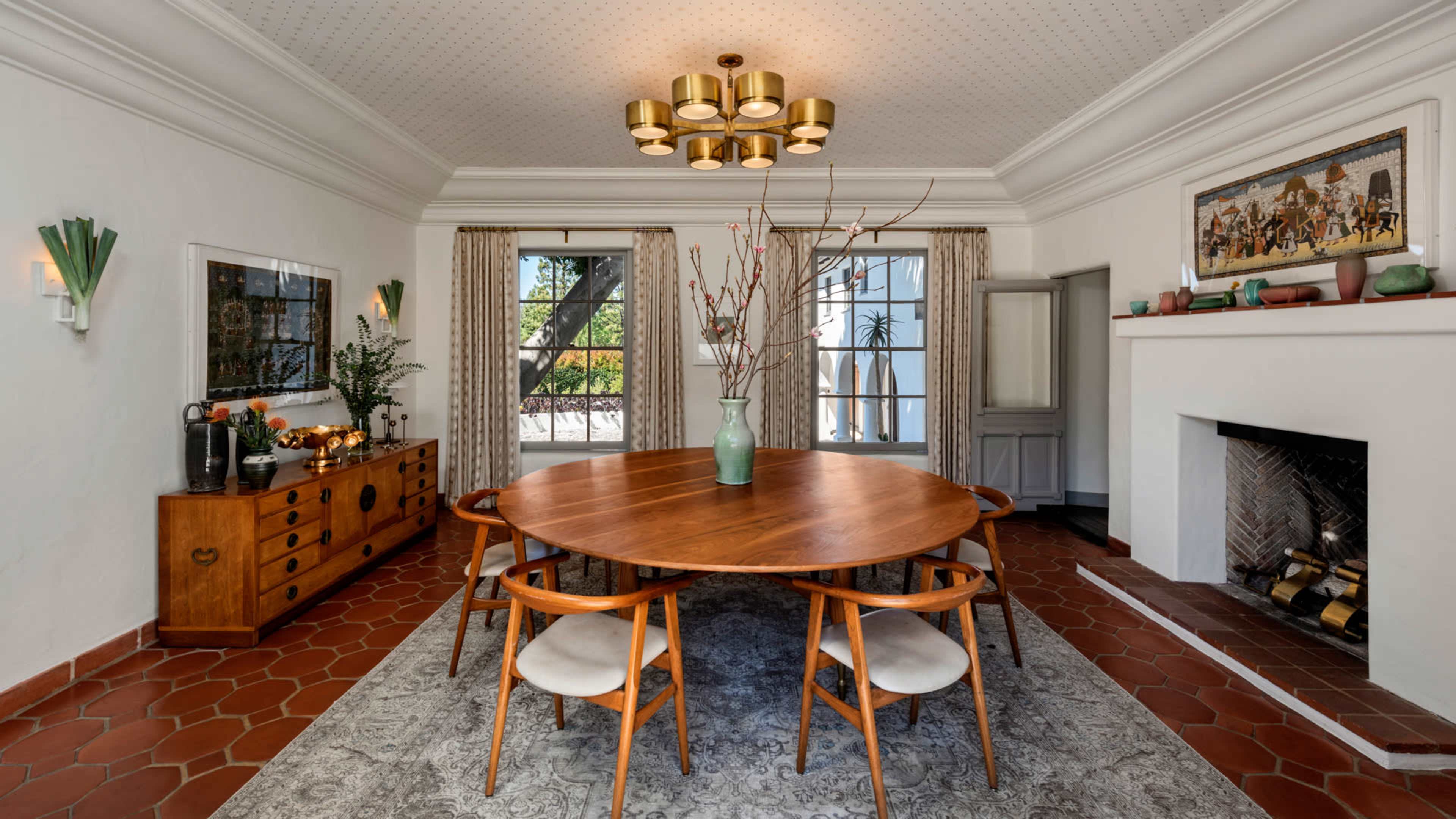 The dining room features a round wooden table surrounded by four chairs, a large fireplace, and double doors leading to an outdoor area.