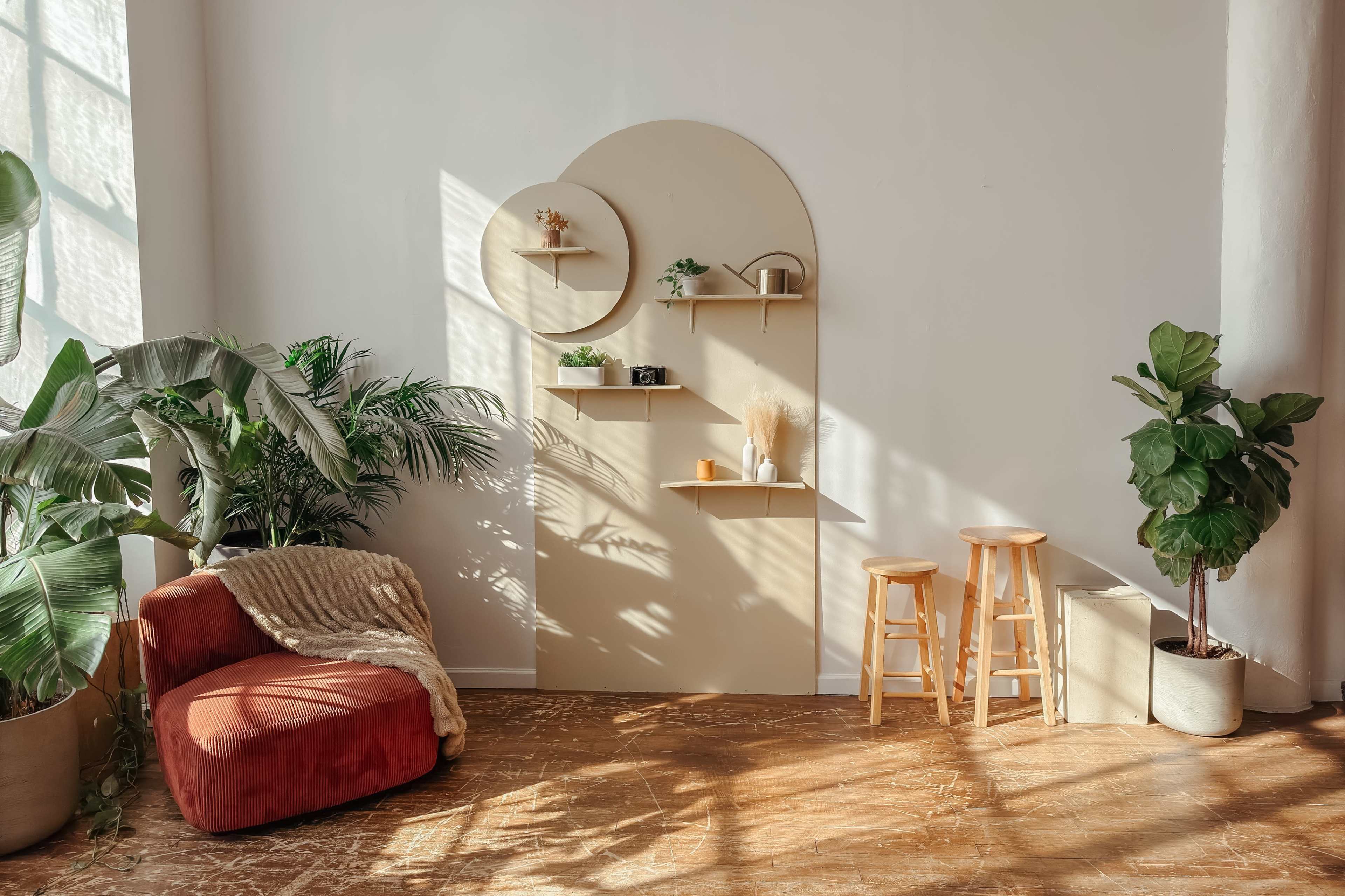 The image shows a cozy interior space featuring a red armchair, wooden stools, a shelf unit against the wall, and various plants.
