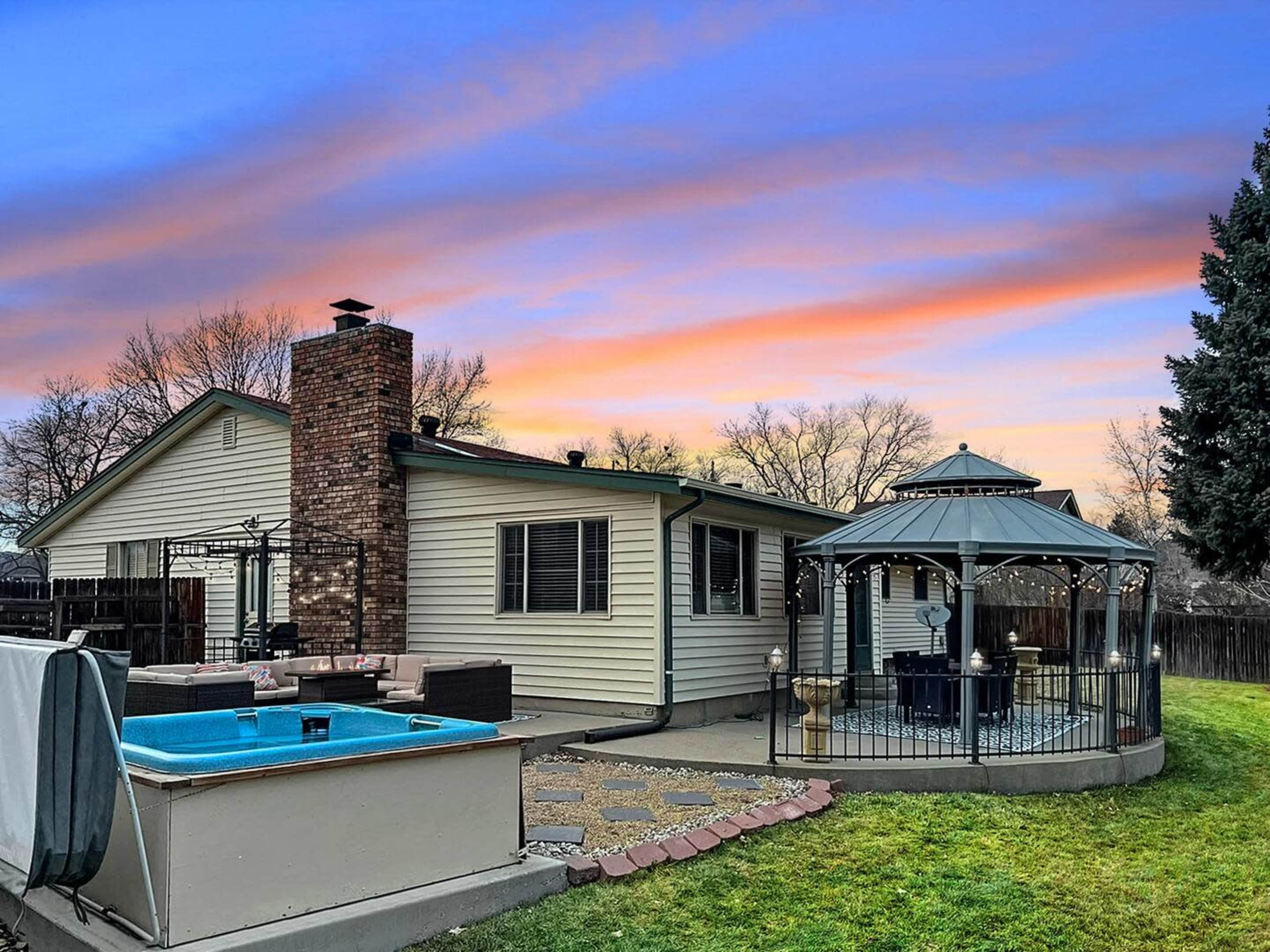 A backyard scene features a rectangular pool, a gazebo, and a house with a brick chimney against a colorful sunset sky.