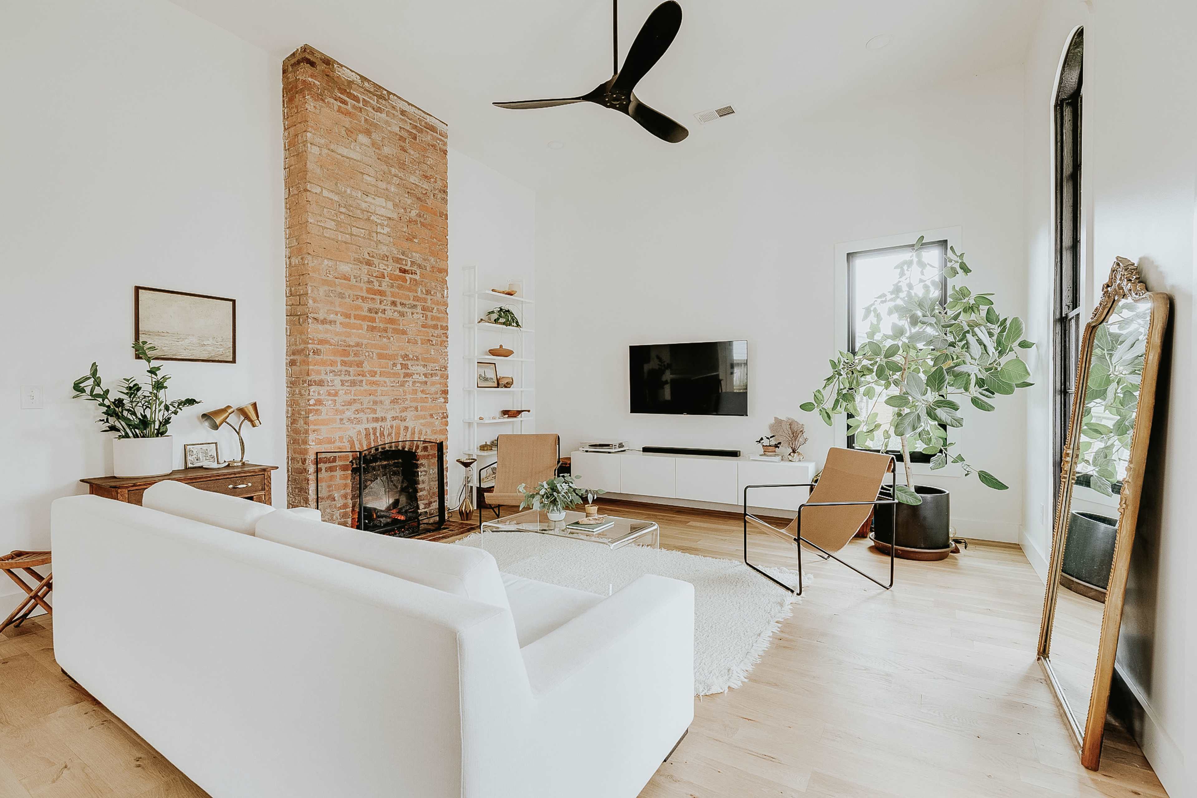 A modern living room featuring a white sofa, a brick fireplace, and a large indoor plant beside a television.