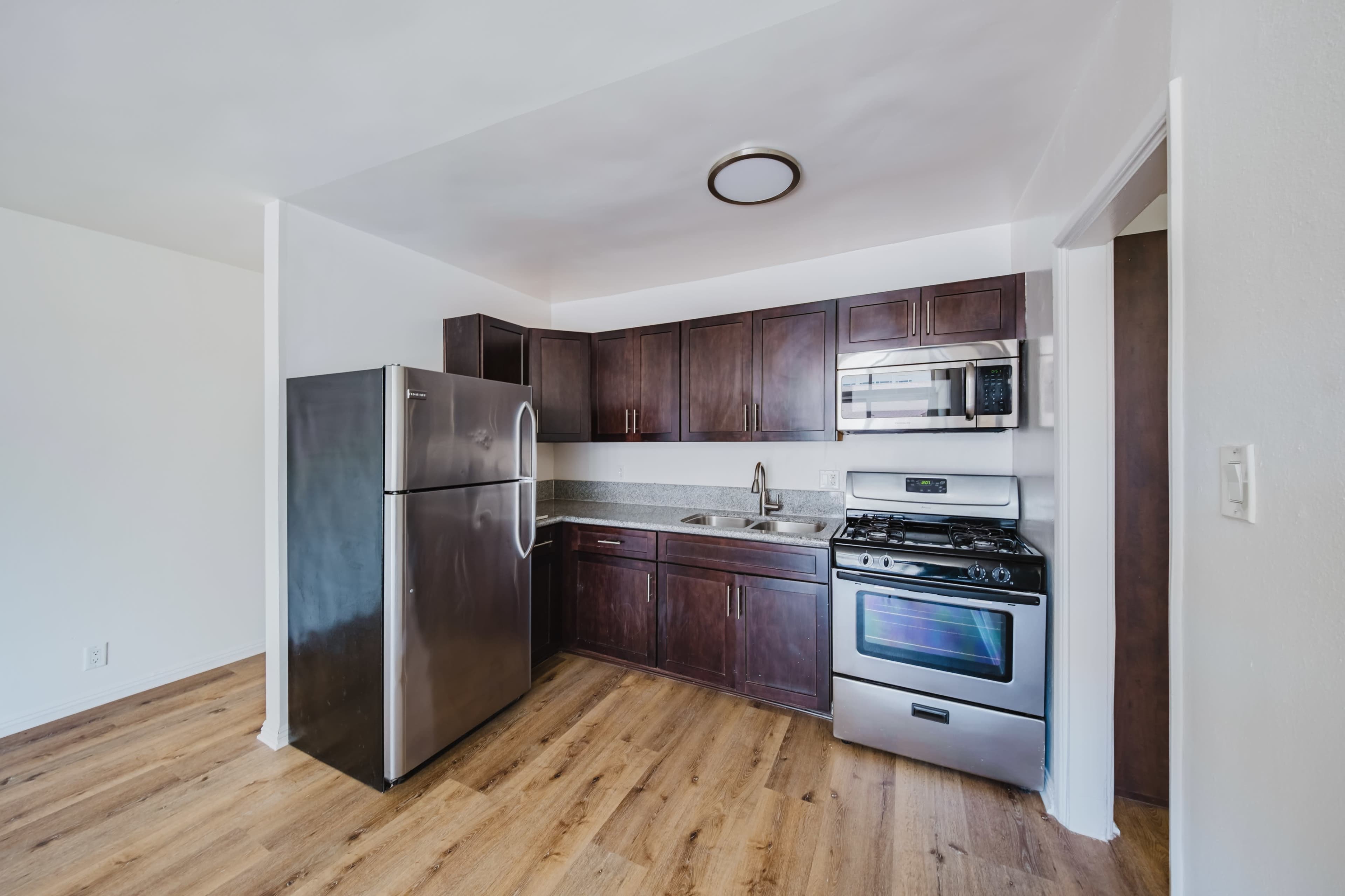The image shows a modern kitchen with dark wooden cabinets, stainless steel appliances, and a countertop.