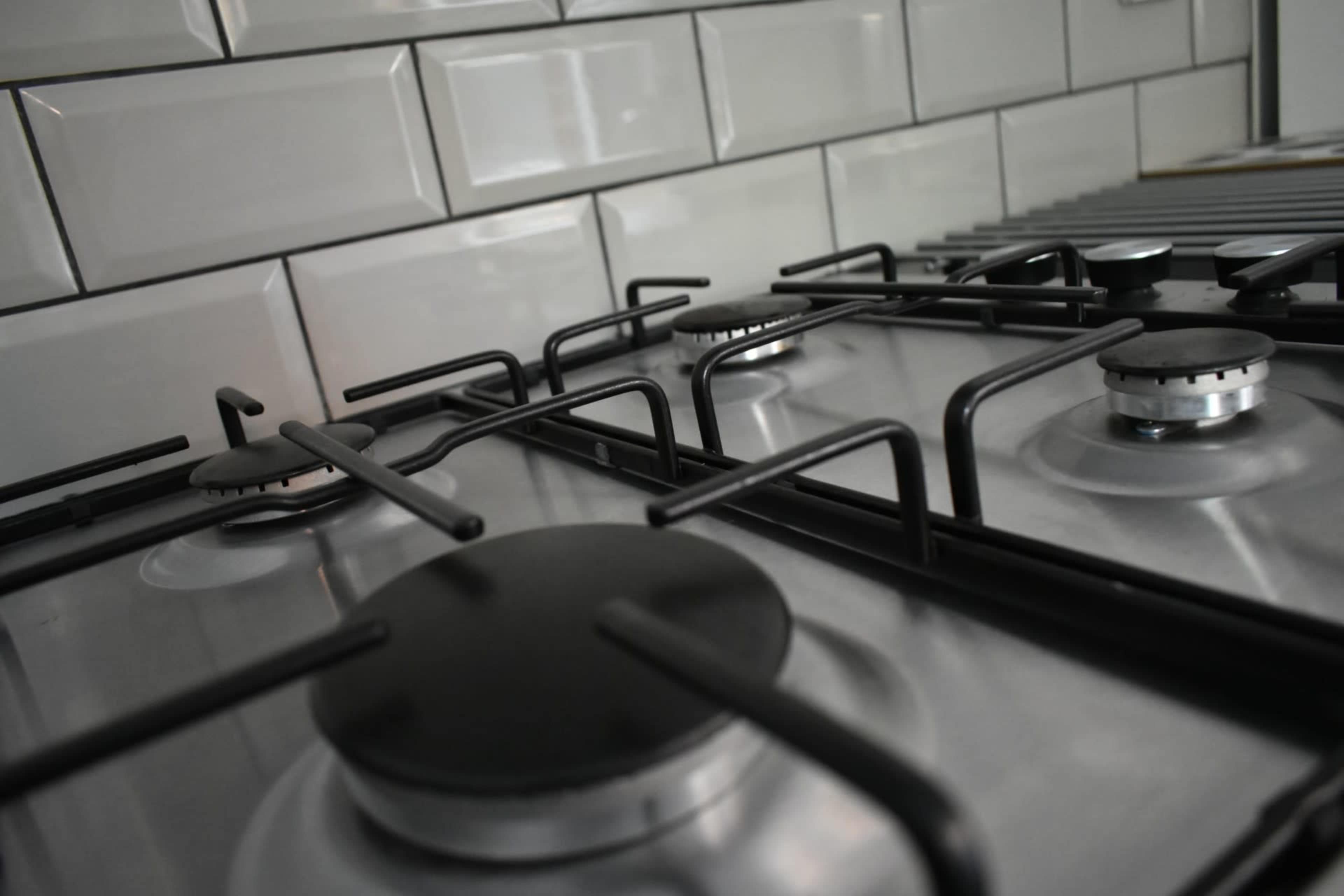 A close-up view of a stainless steel gas cooktop with black knobs and grates, set against a tiled backsplash.