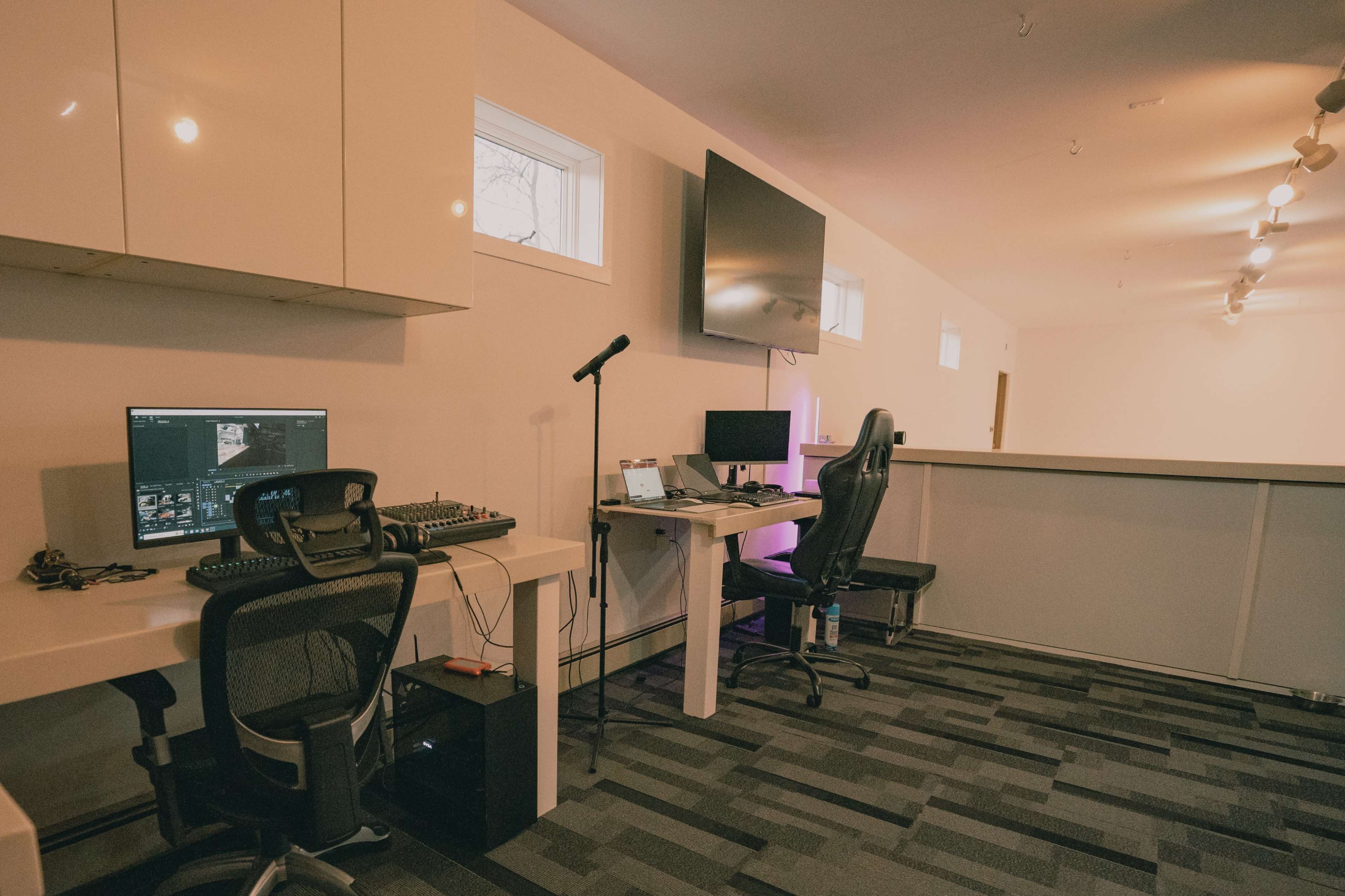 A modern office space with two desks equipped with computers and audio equipment, and a large television mounted on the wall.