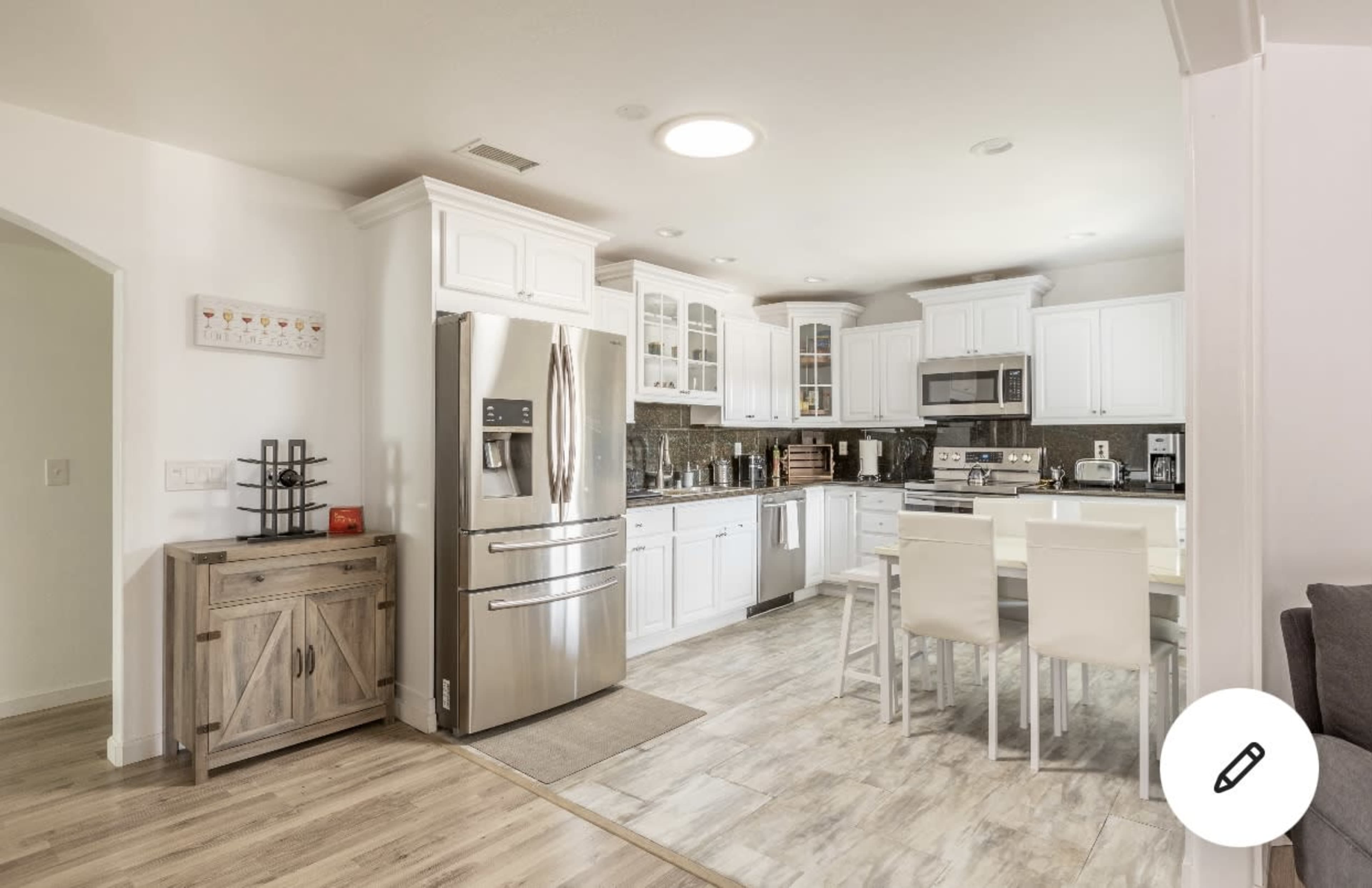 A modern kitchen features white cabinetry, stainless steel appliances, and a dining table with white chairs.