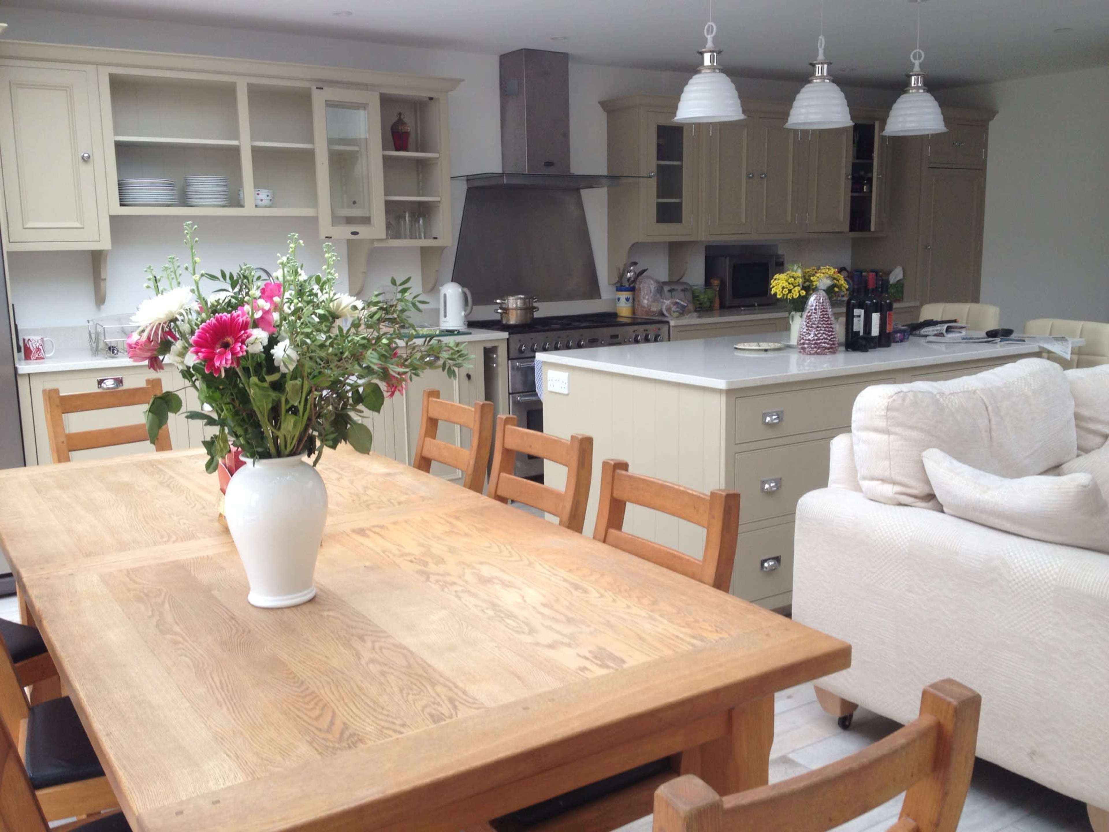 A spacious kitchen features a wooden dining table with flowers, a large oven range, and light-colored cabinetry.