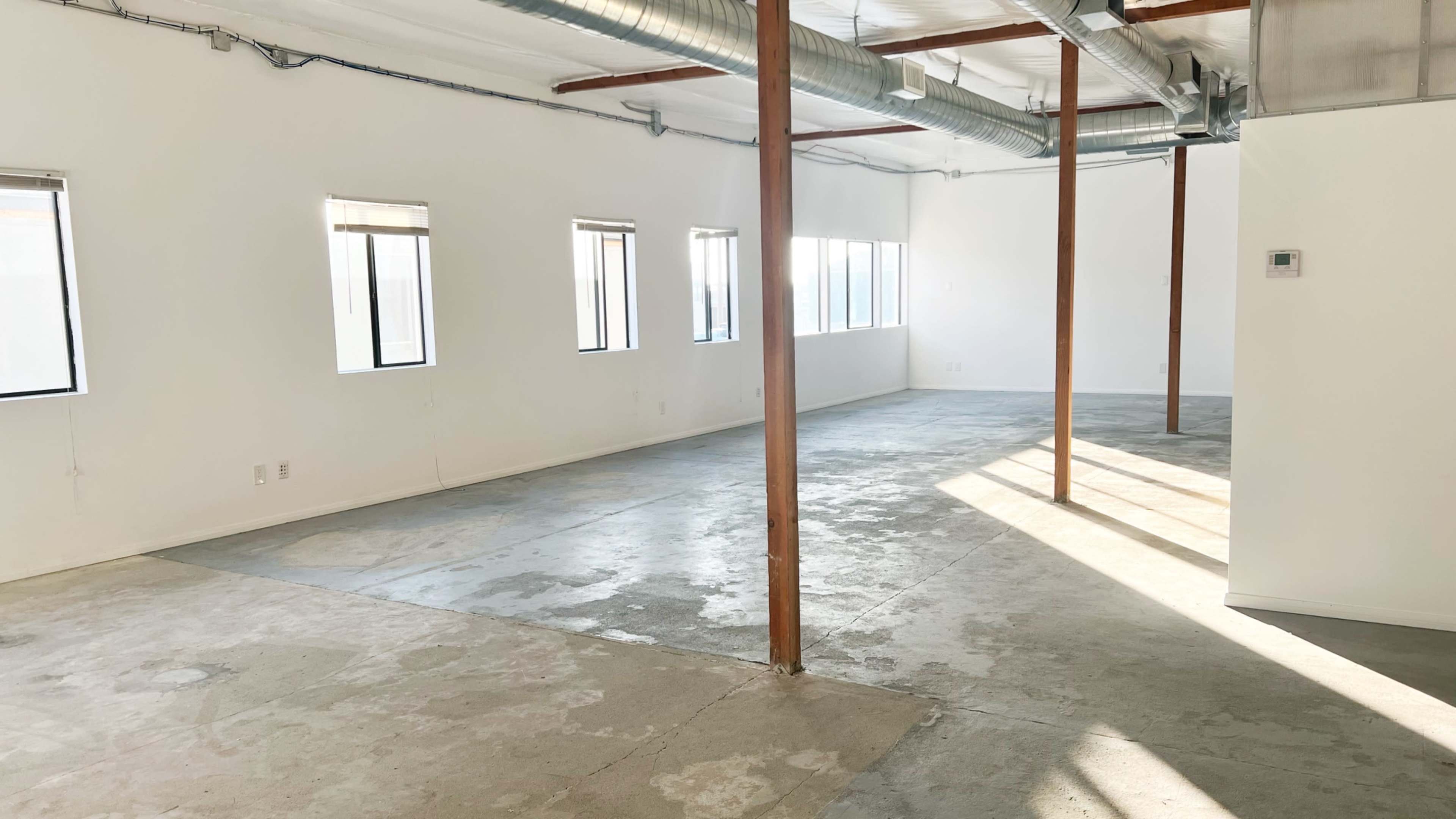 An empty room with concrete flooring, large windows, and exposed wooden beams.