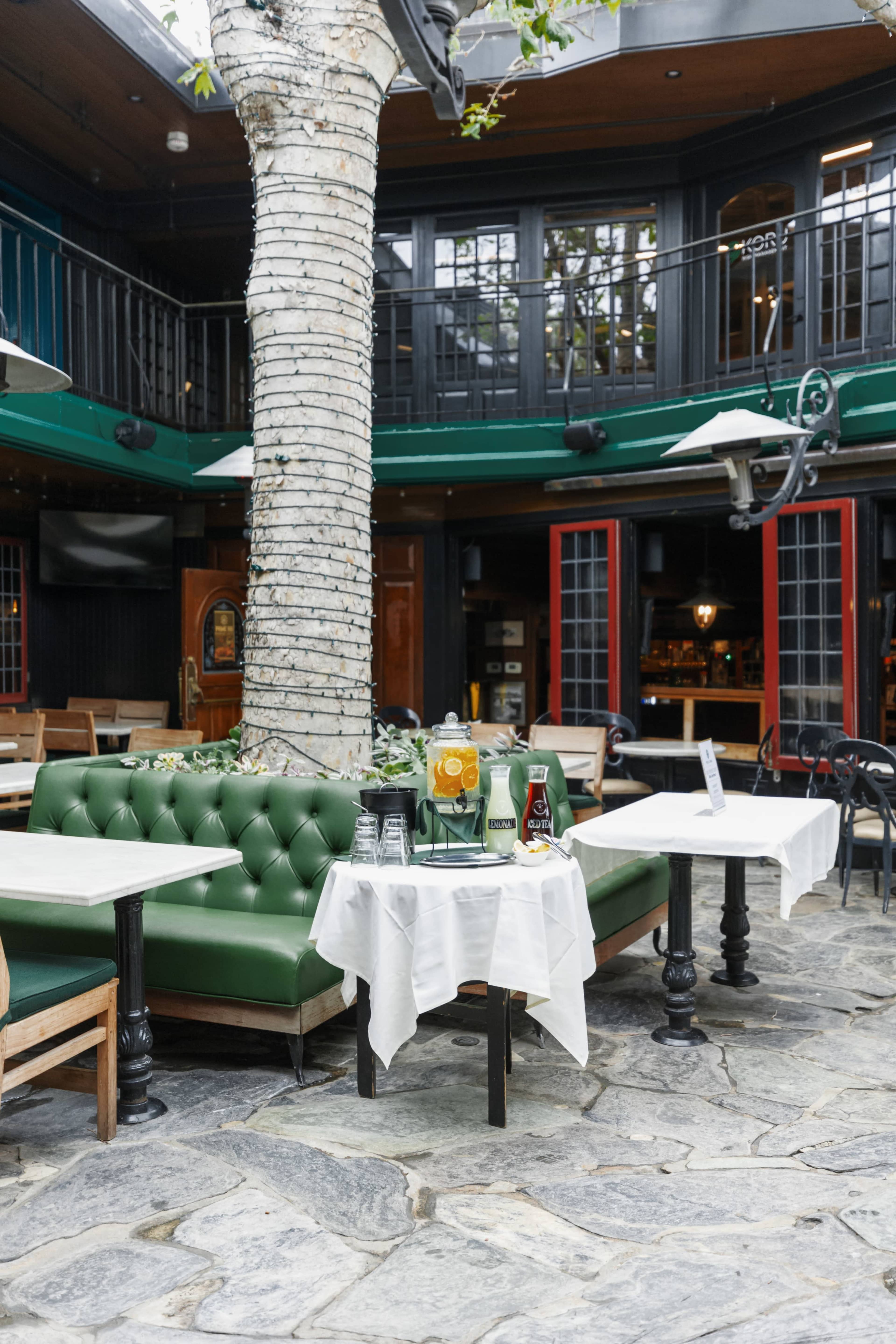 A green cushioned seating area with tables is set up around a large tree in a restaurant's open space.