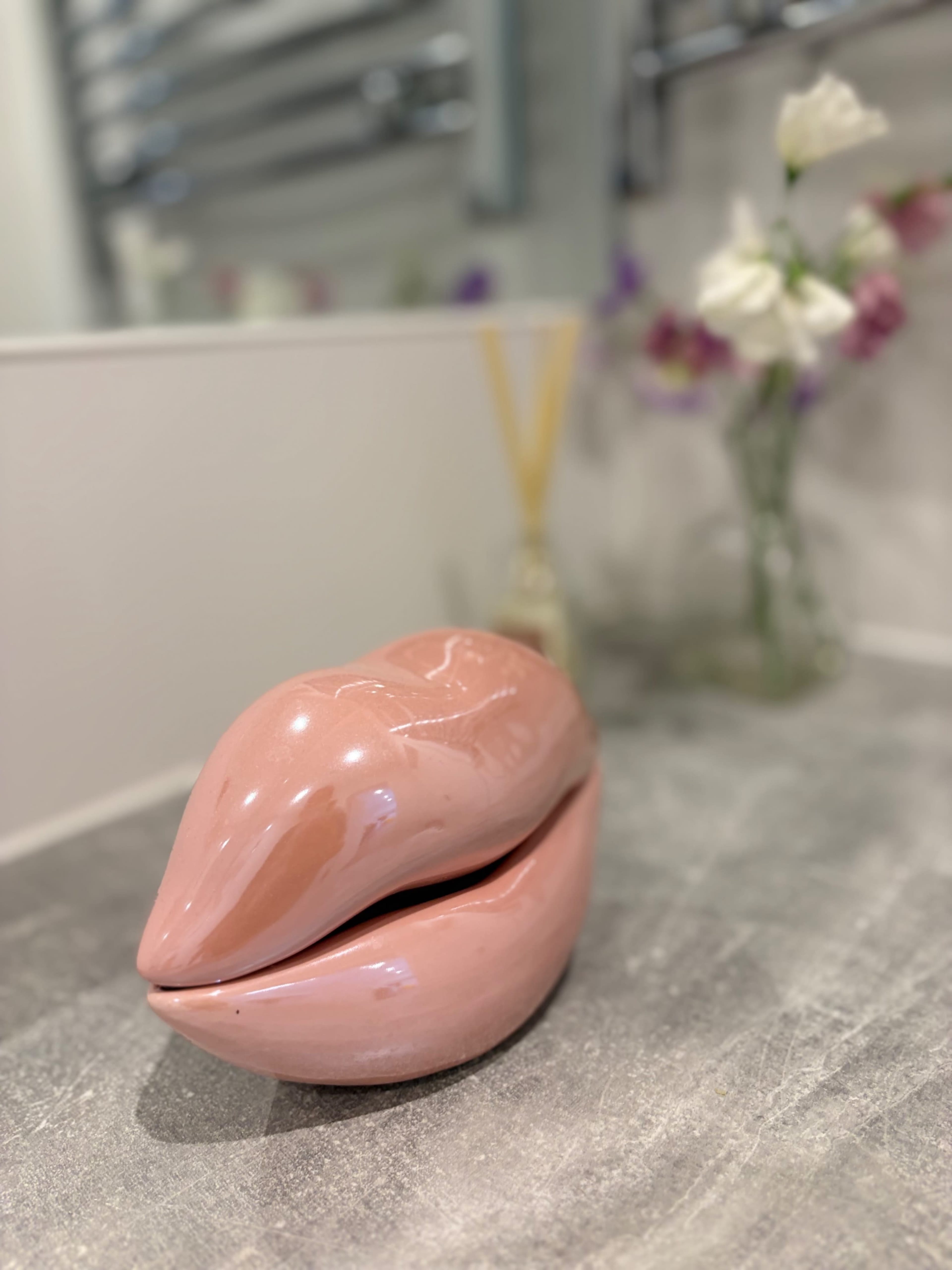 A glossy pink ceramic object shaped like lips is placed on a countertop next to a vase of flowers.
