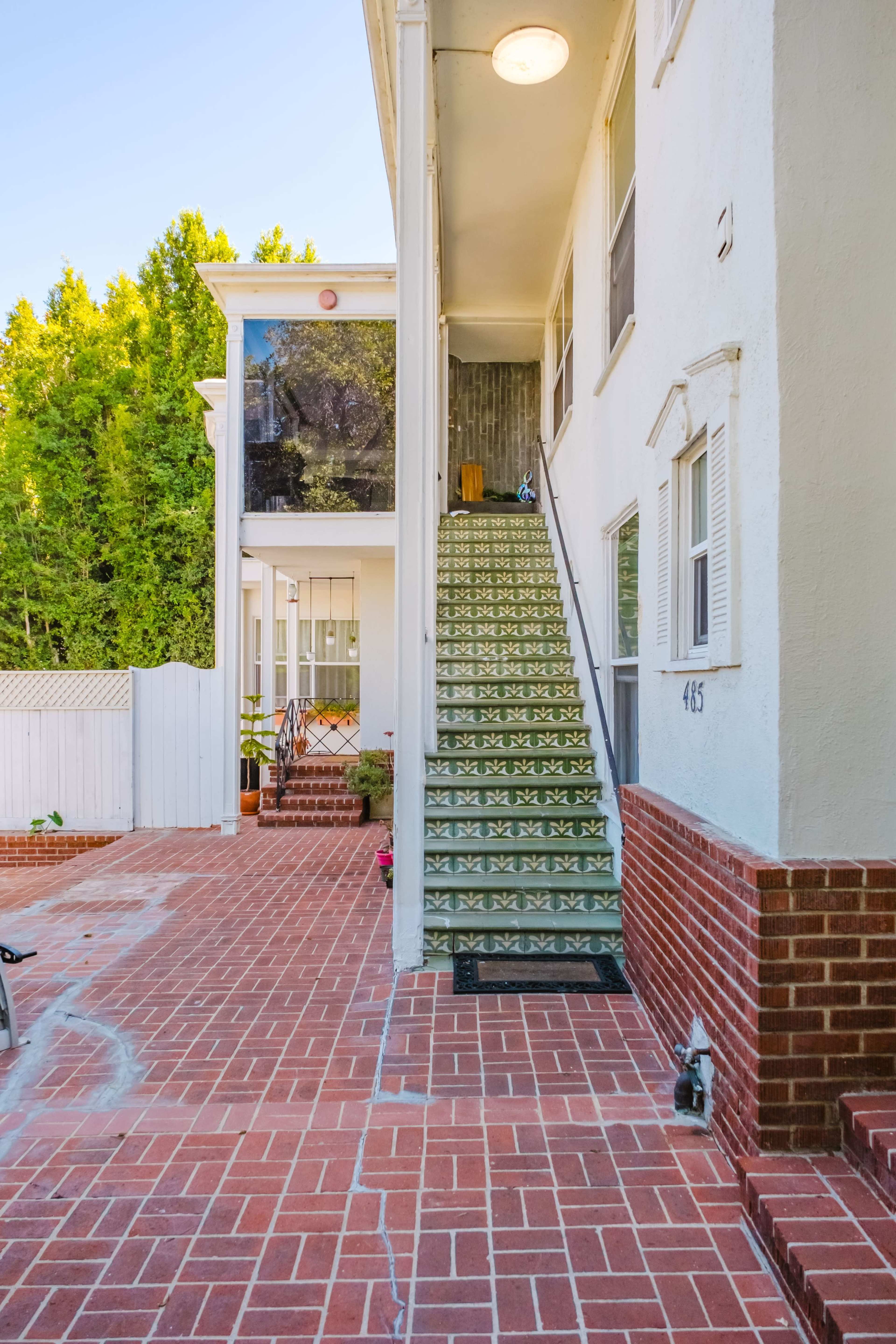 The image shows a brick-paved courtyard leading to a two-story building with a staircase covered in decorative tiles.