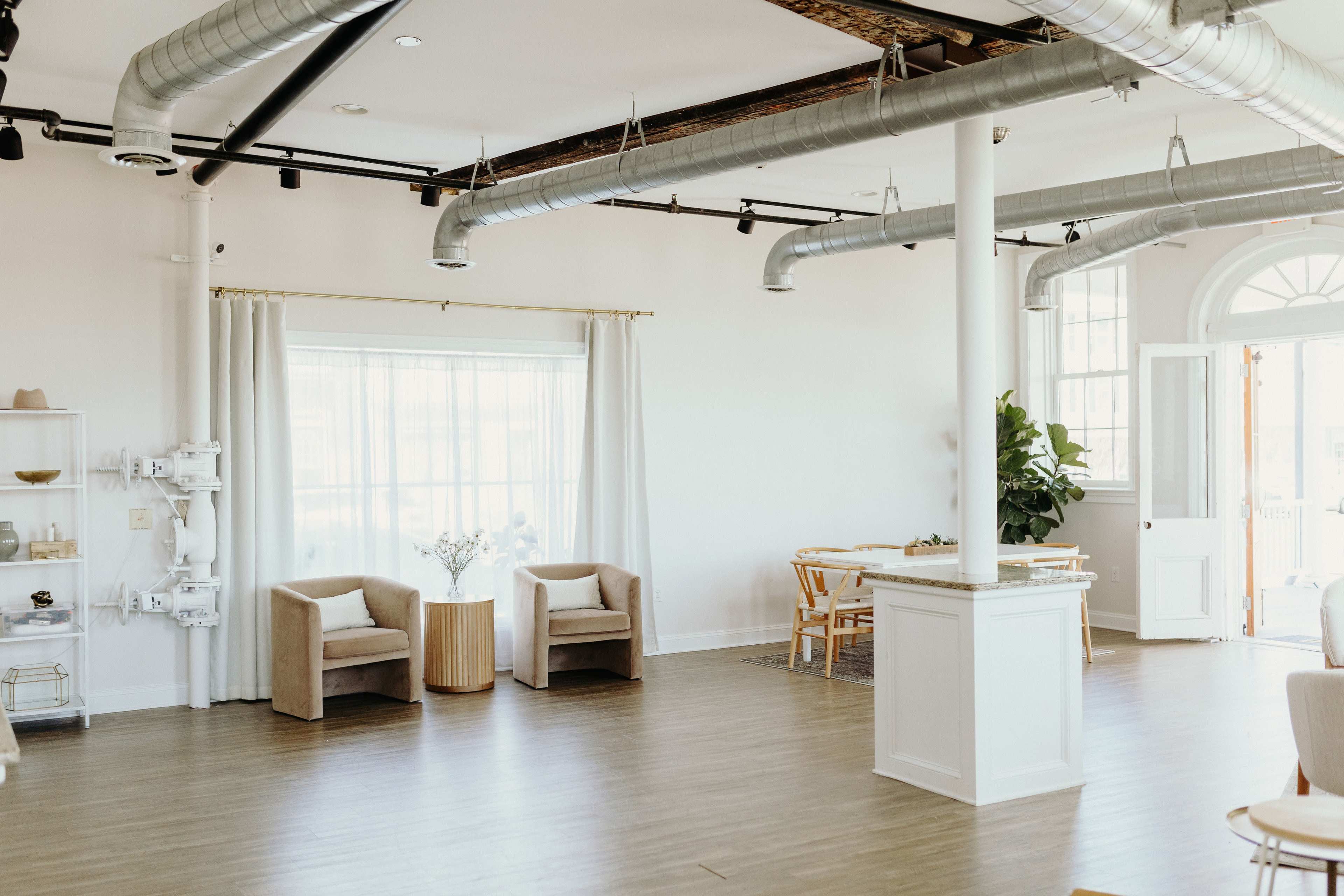 A spacious, well-lit room with two chairs, a small table, and natural daylight filtering through sheer curtains.