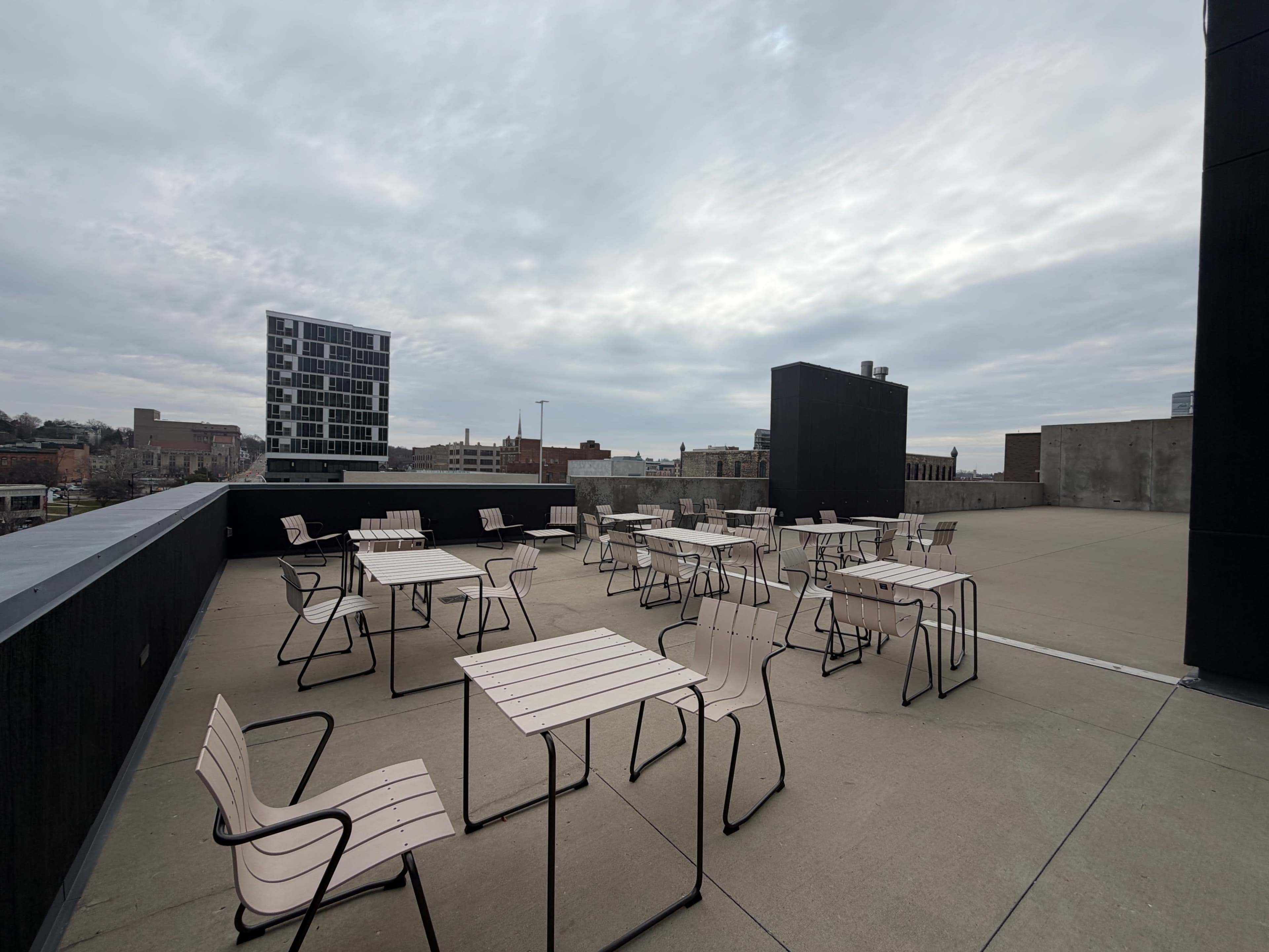 The rooftop area features several tables and chairs arranged on a concrete surface under a cloudy sky.