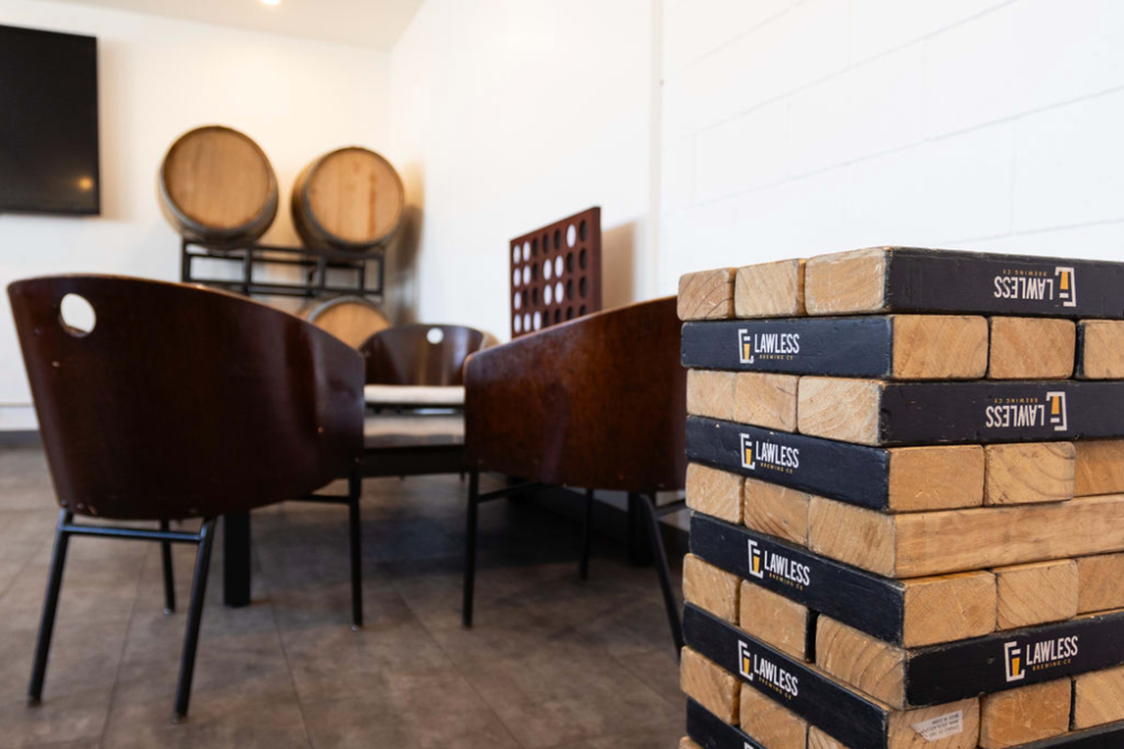 A stack of wooden blocks labeled "Lawless" is positioned in the foreground of a room featuring chairs and wine barrels in the background.