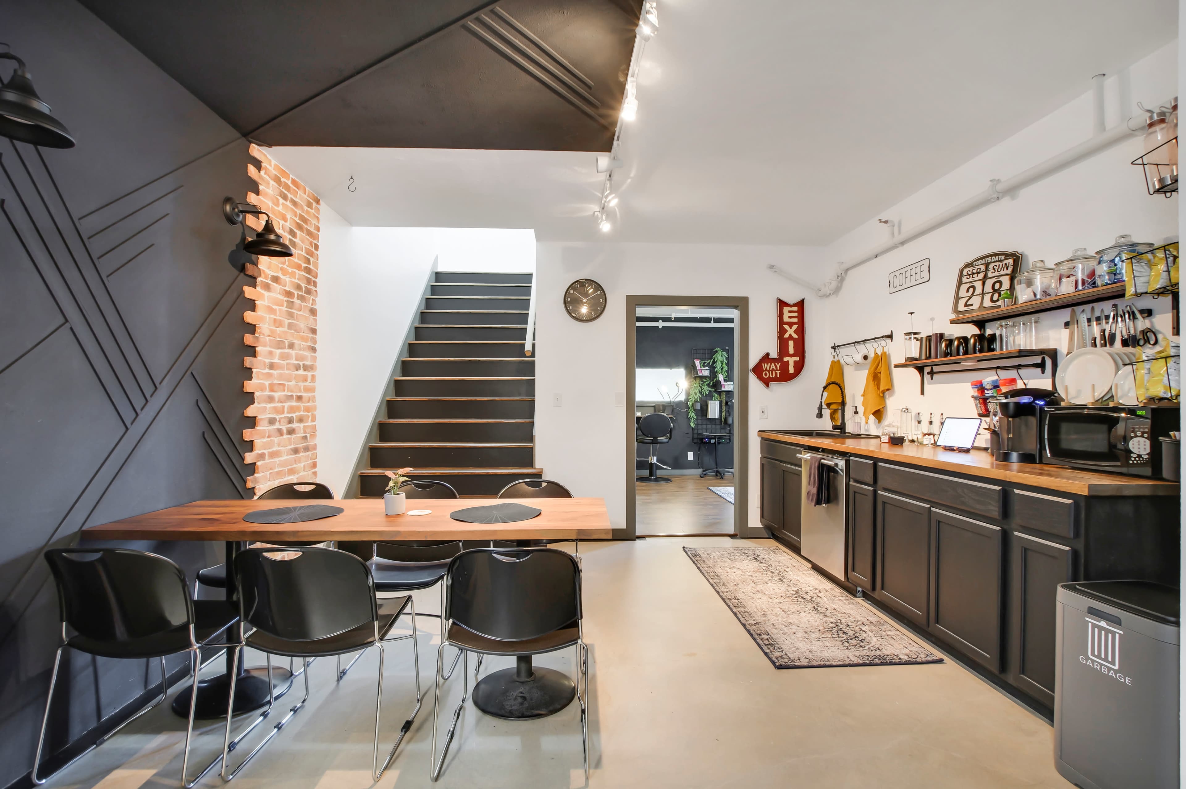A modern kitchen and dining area with a wooden table, black chairs, and a staircase leading to an upper level.