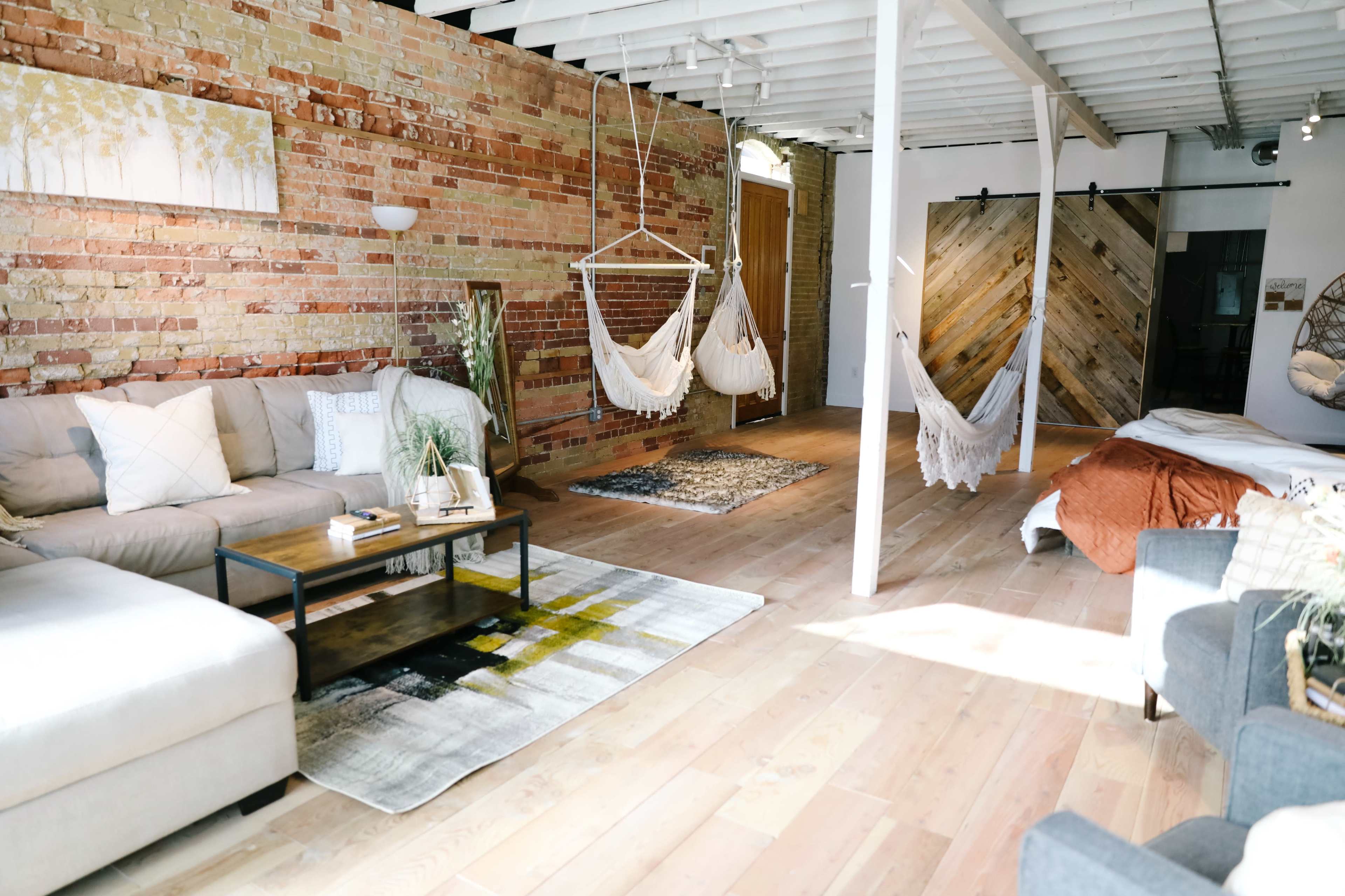 A spacious, well-lit living area featuring a sectional sofa, hanging hammocks, and a wooden accent wall.