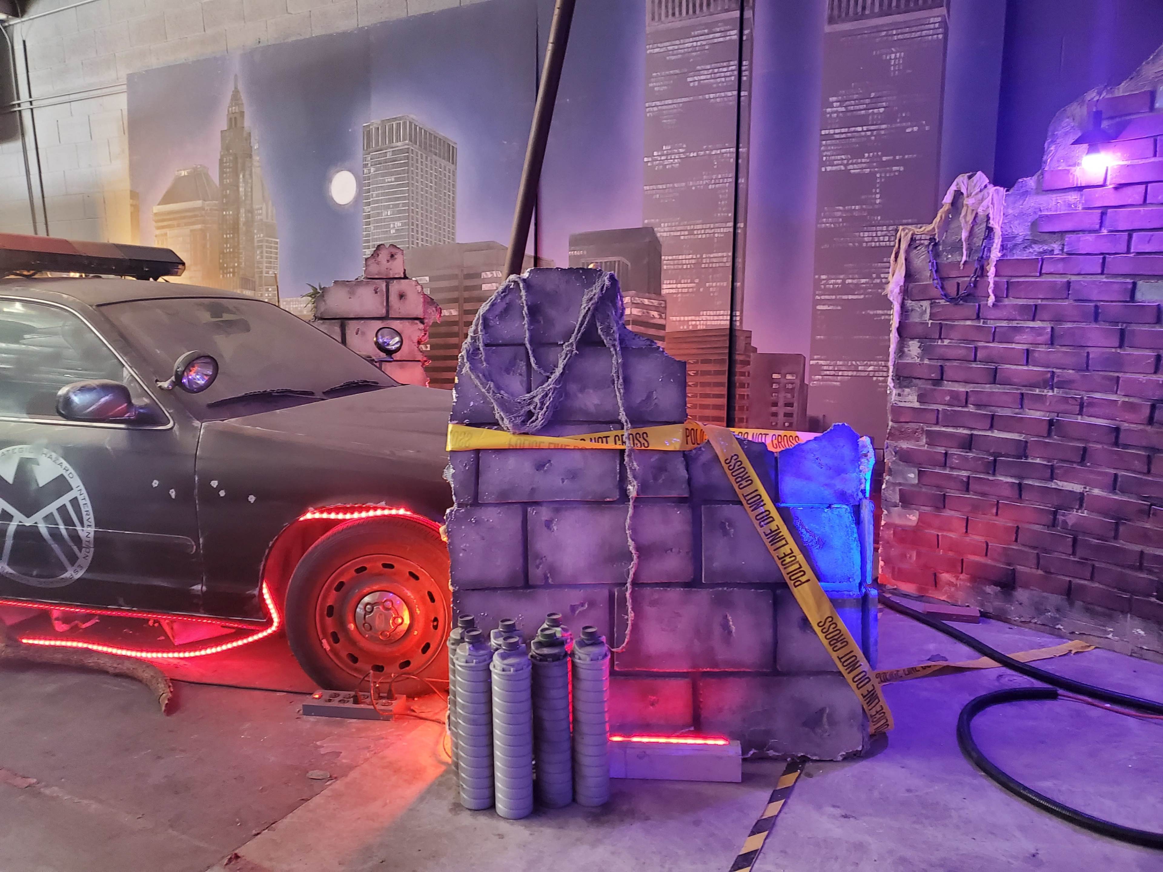 A partially constructed display featuring a car with a shield emblem, surrounded by broken wall replicas and decorative lighting.