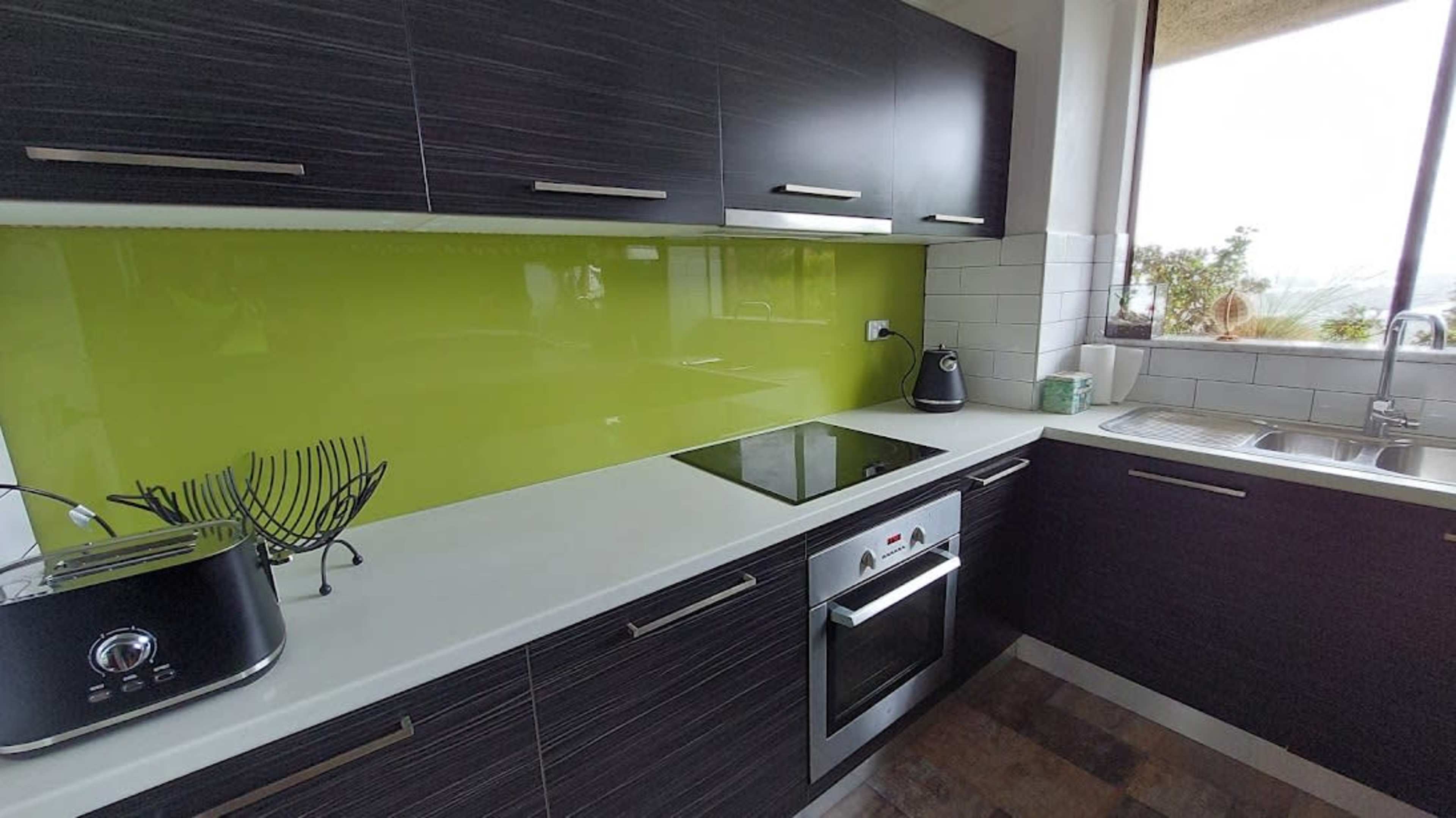 A modern kitchen with dark wooden cabinets, a bright green backsplash, and stainless steel appliances.