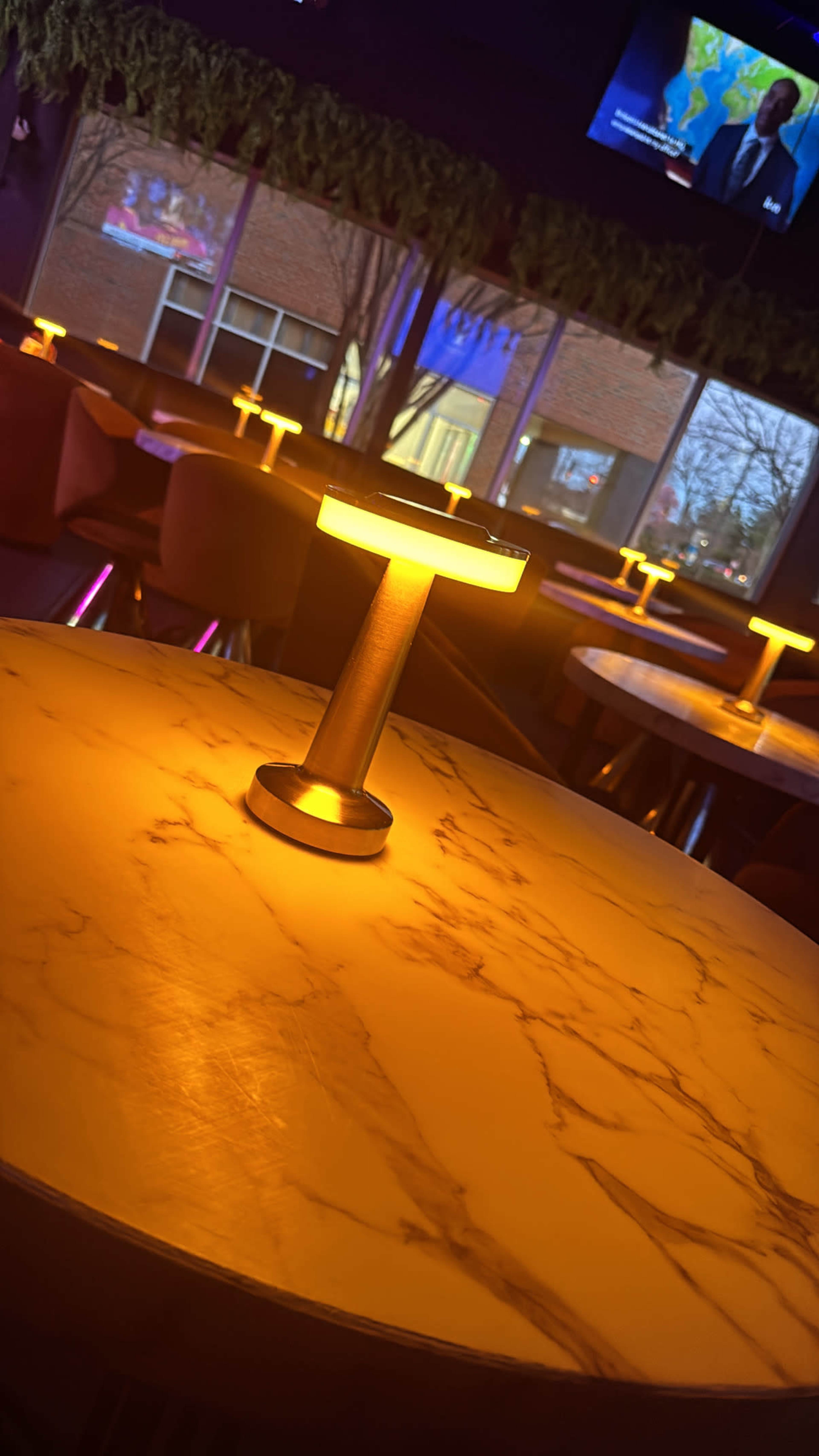 The image shows a dimly lit restaurant interior with a marble table and illuminated table lamps arranged around the space.